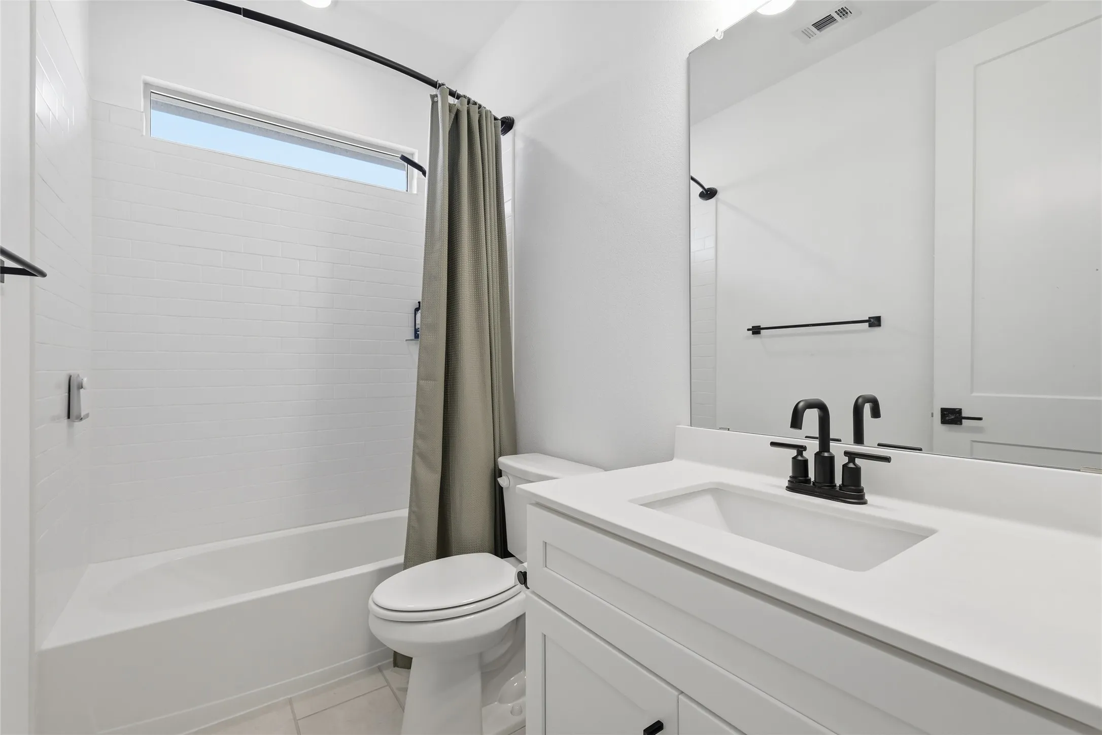 Bathroom featuring a white subway tile tub surround, transom window, white vanity with integrated sink, matte black hardware, and an expansive wall mirror