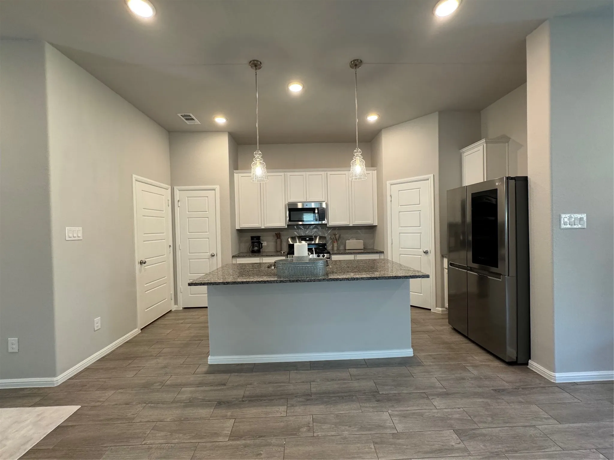 Contemporary kitchen featuring a spacious island with a speckled countertop, white cabinetry, recessed lighting, and wood-finish flooring