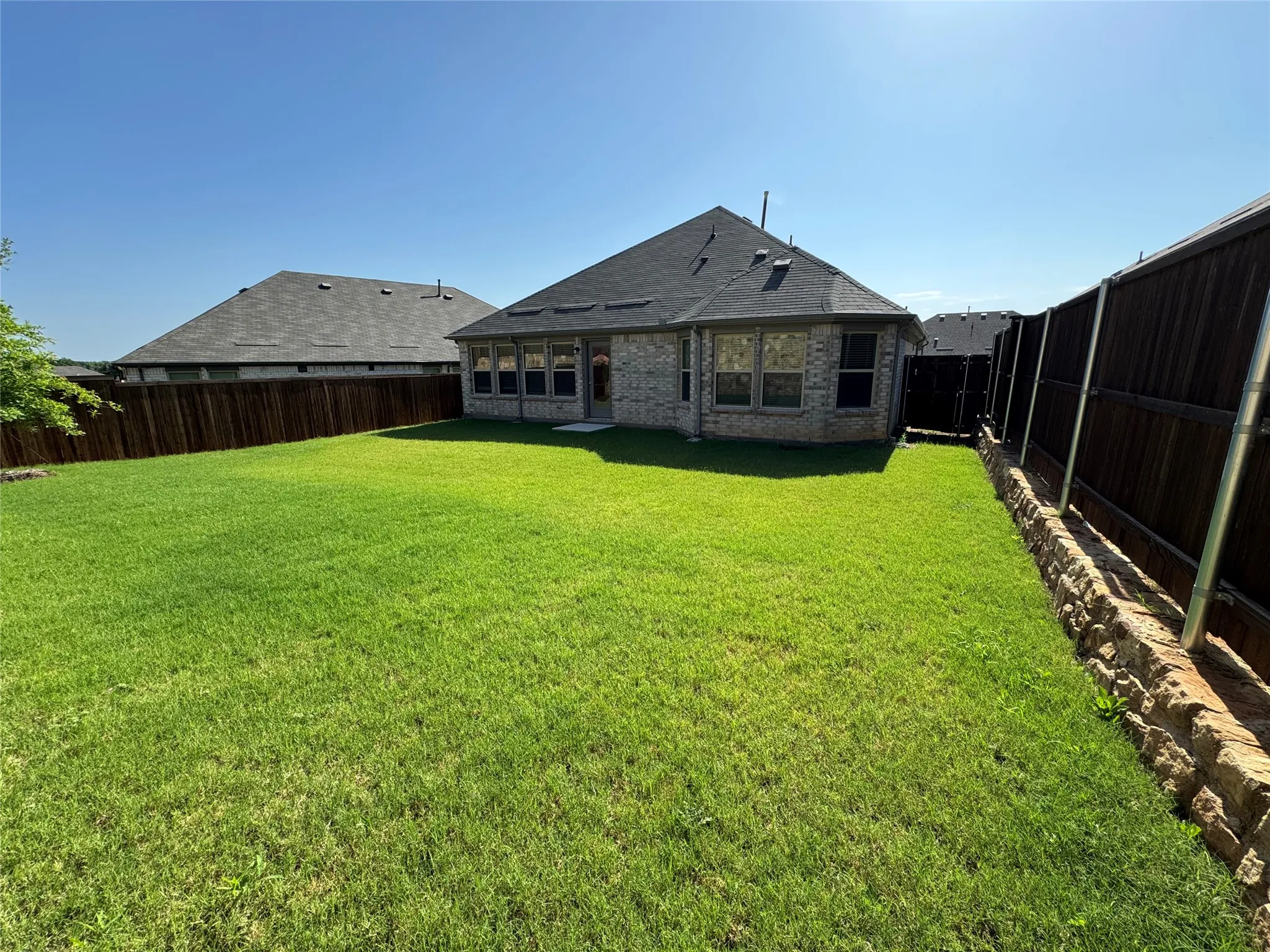 Expansive backyard featuring a manicured lawn, full privacy fencing, and a stone retaining wall