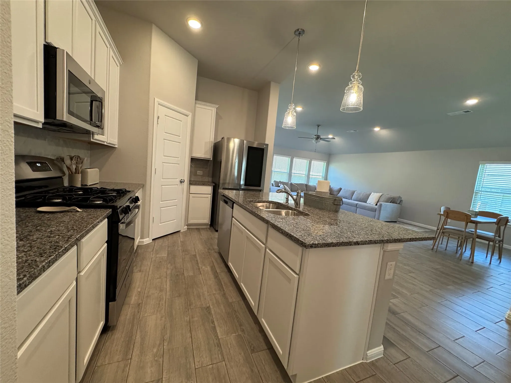 Spacious kitchen featuring granite countertops, stainless steel appliances, wood-finish flooring, white cabinetry, and an island with a double sink