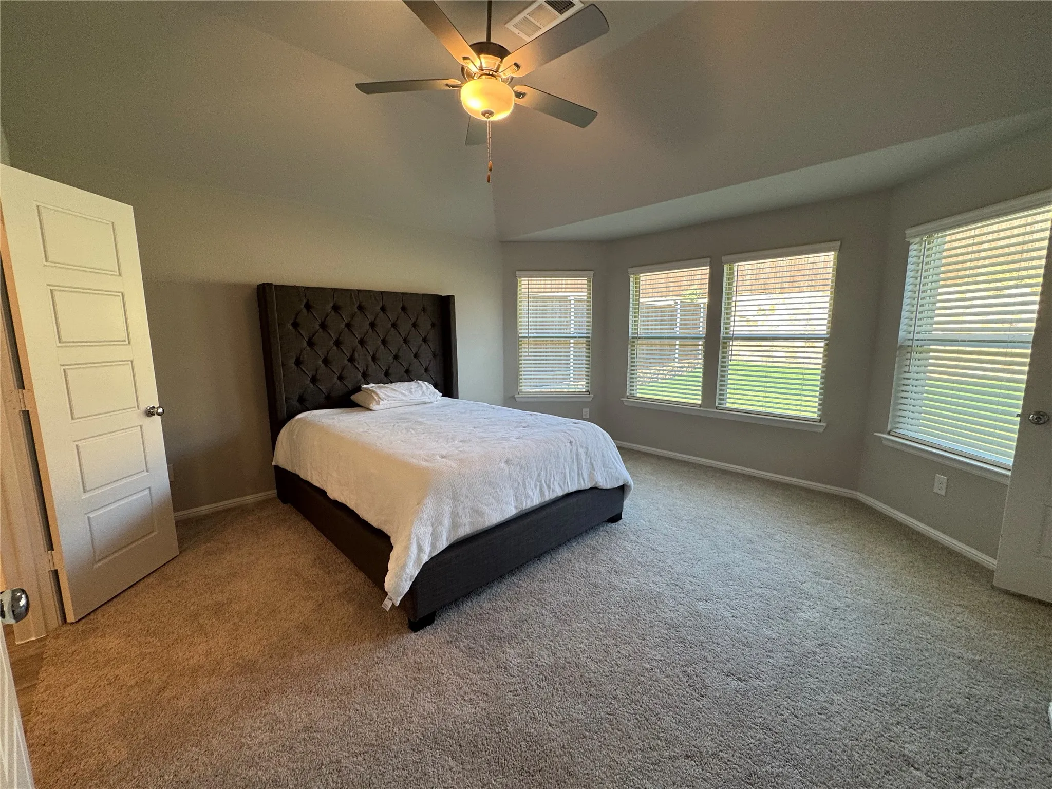 Carpeted bedroom featuring a vaulted ceiling with a ceiling fan, a bay window with multiple panes, and paneled doors