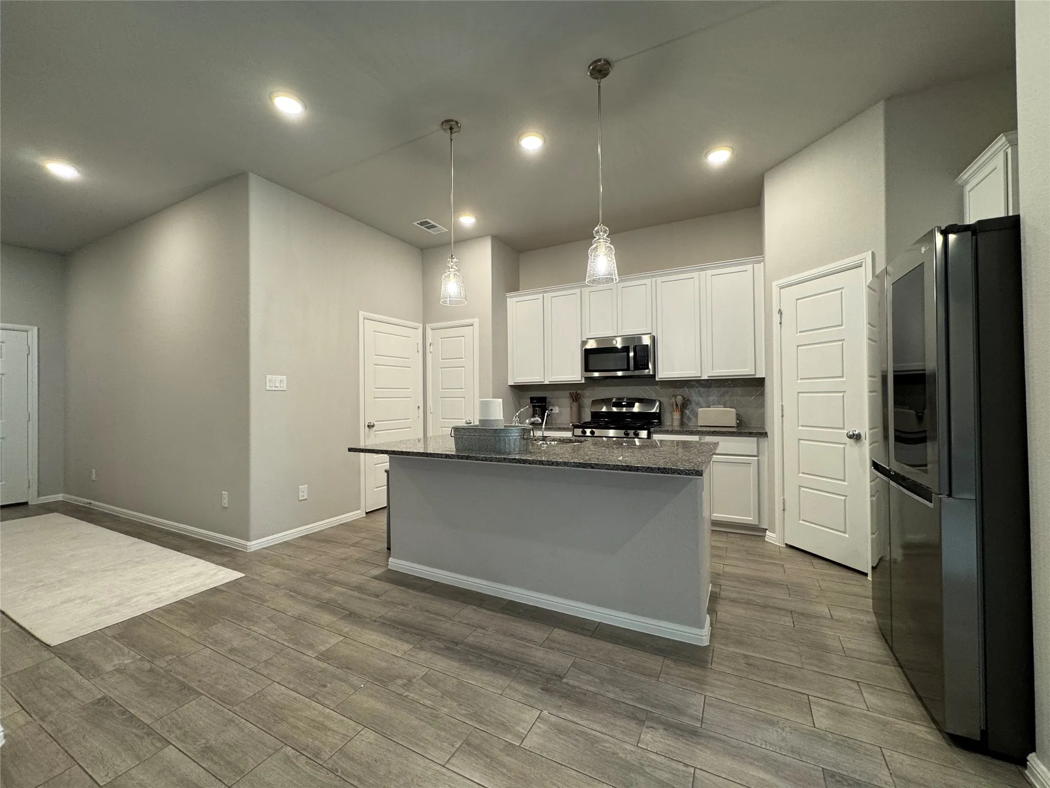 Modern kitchen featuring a central island with a dark countertop, white shaker-style cabinetry, stainless steel appliances, recessed lighting, and wood-finish flooring