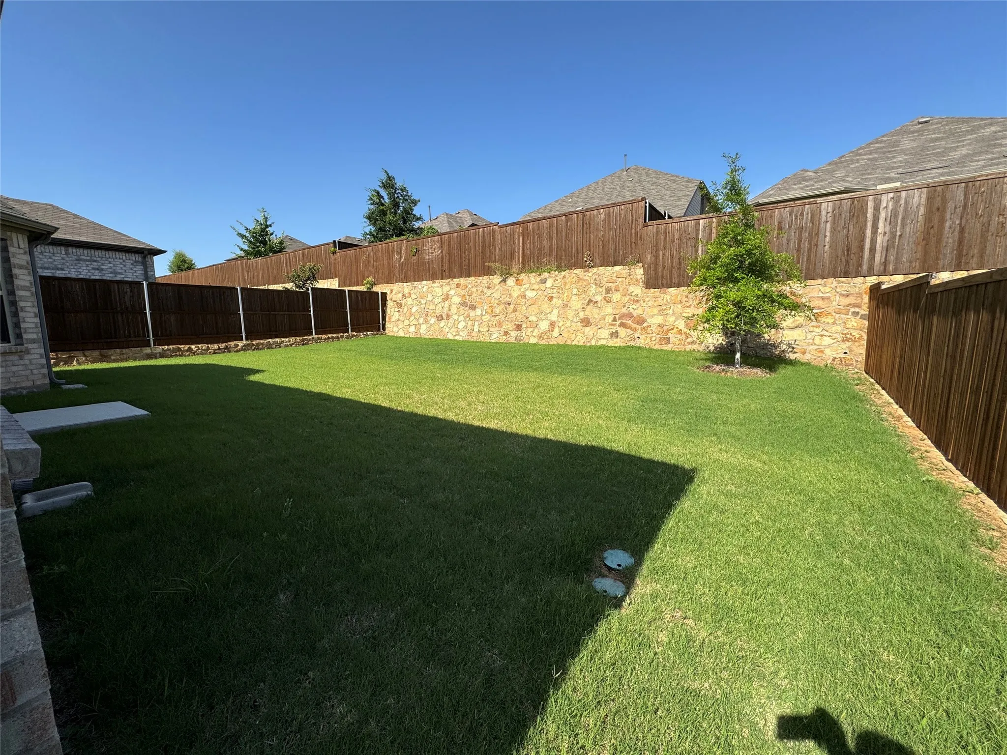 Spacious backyard featuring extensive green lawn, a stone retaining wall, and a wood privacy fence