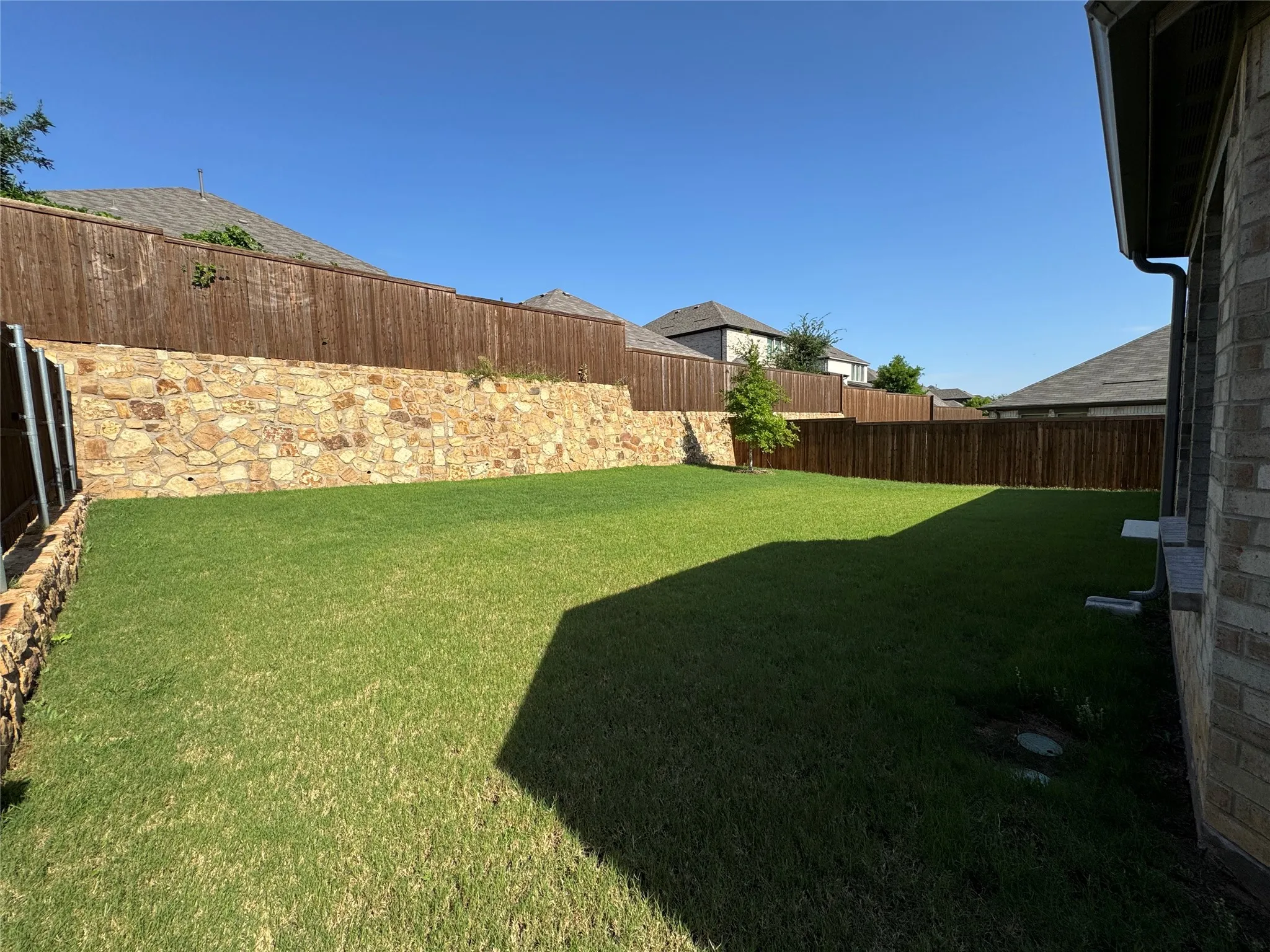 Expansive grass lawn featuring a stone retaining wall and full privacy fencing