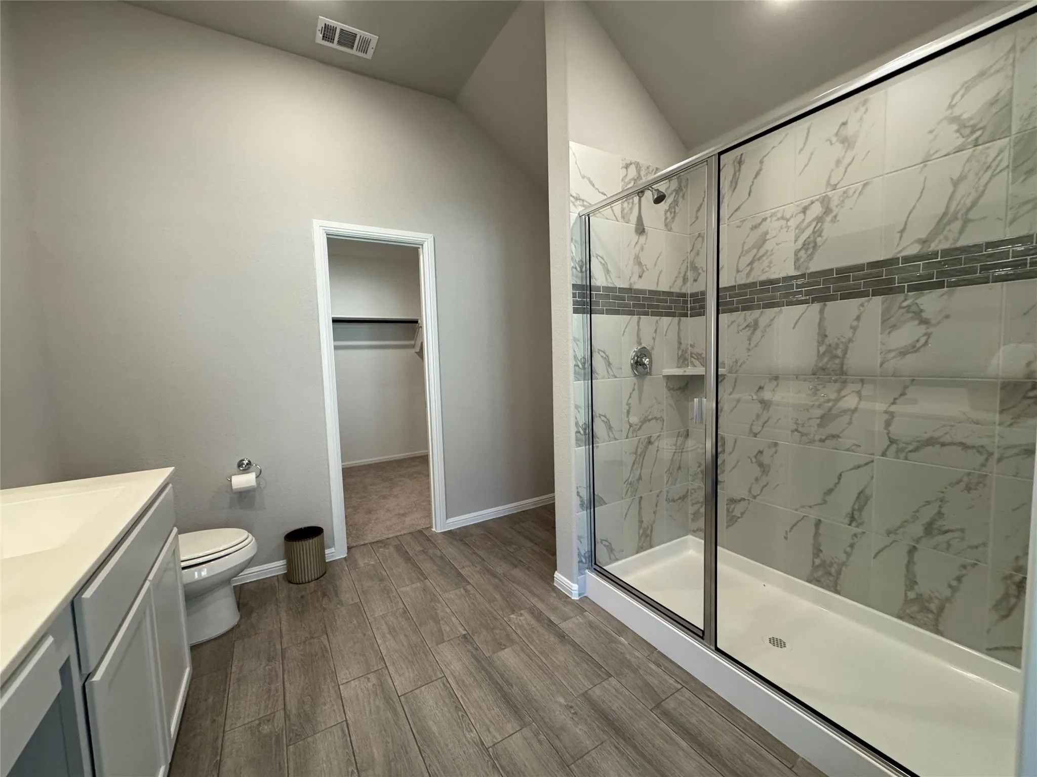Spacious bathroom featuring a glass-enclosed shower with marbled tile, a decorative tile accent band, and a built-in shower niche