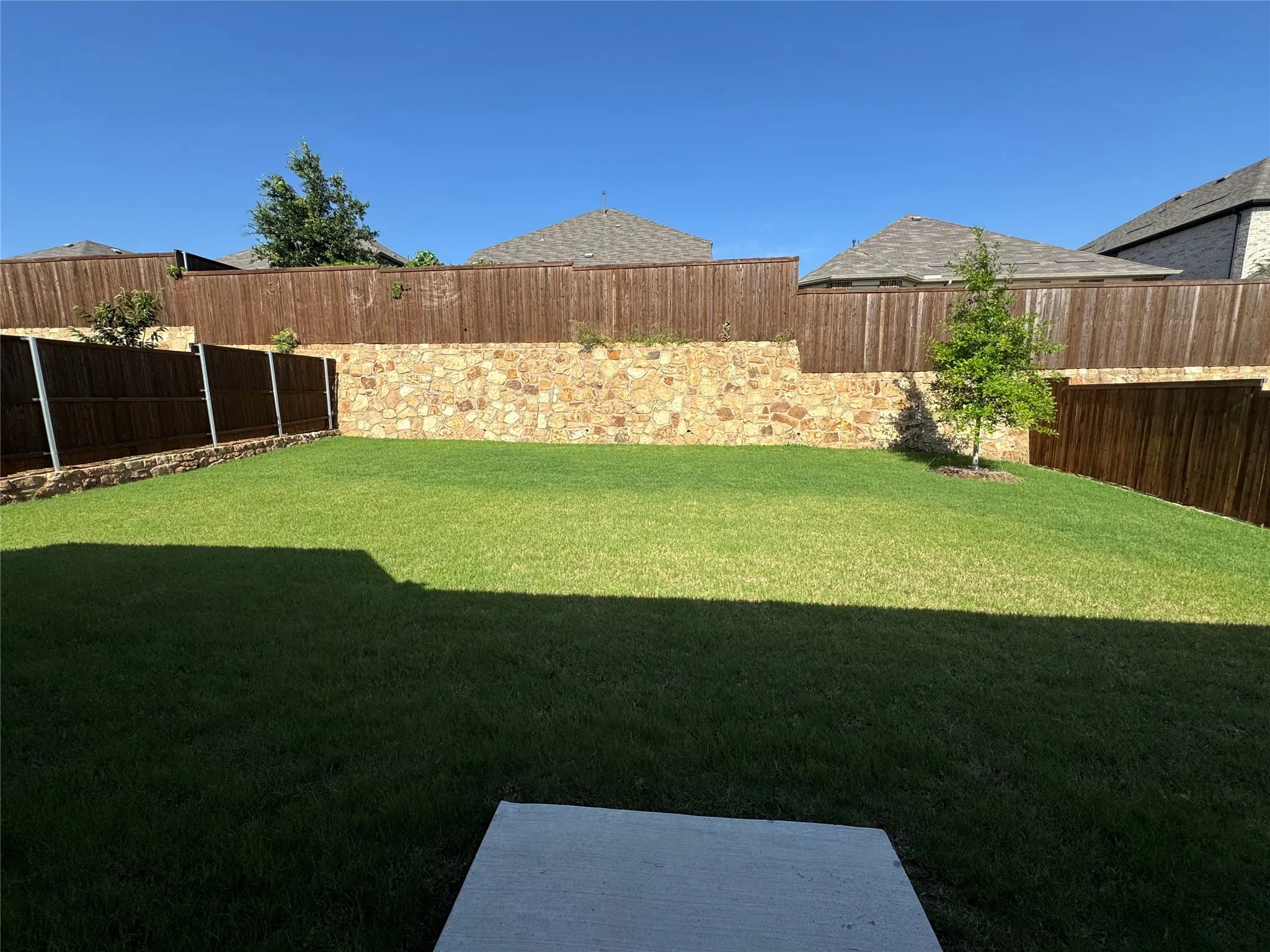 Expansive backyard featuring a large green lawn, stone retaining wall, and wood fencing