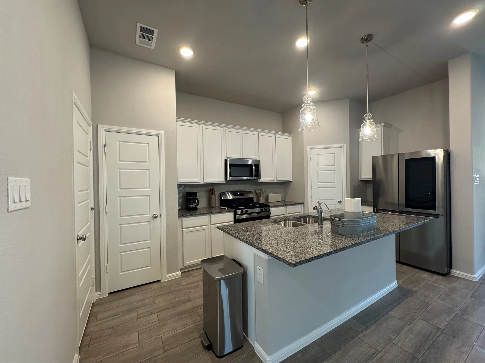 Kitchen featuring an island with granite countertop, stainless steel appliances, white cabinetry, and wood-finish flooring