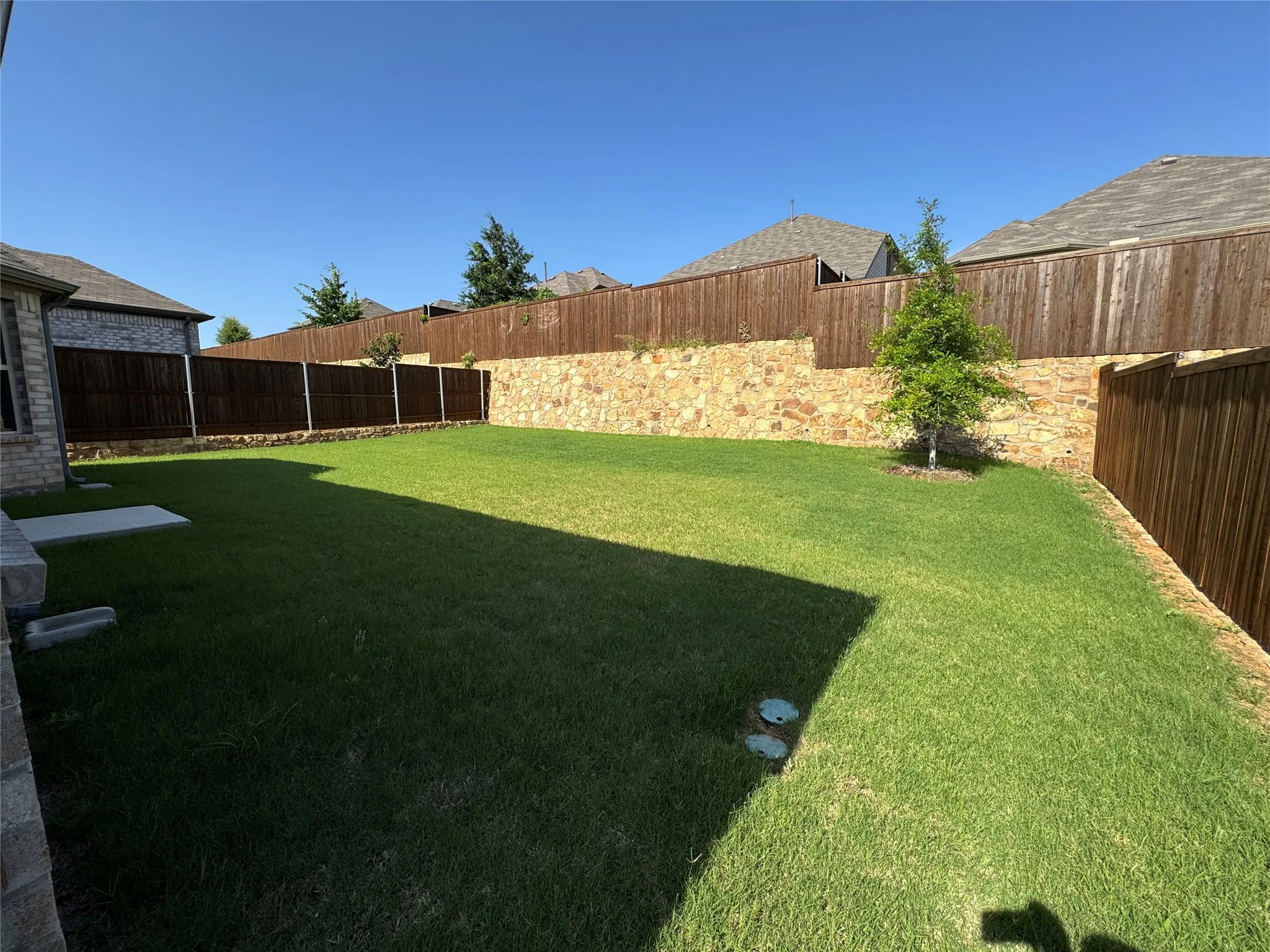 Expansive lawn area featuring a stone retaining wall and a wood privacy fence