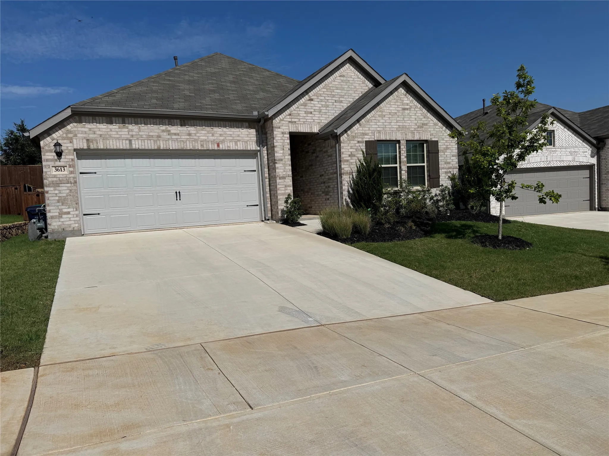 Contemporary single-story residence featuring light-colored brick facade, a two-car garage with modern hardware, dark brown window shutters, and a dark shingle roof