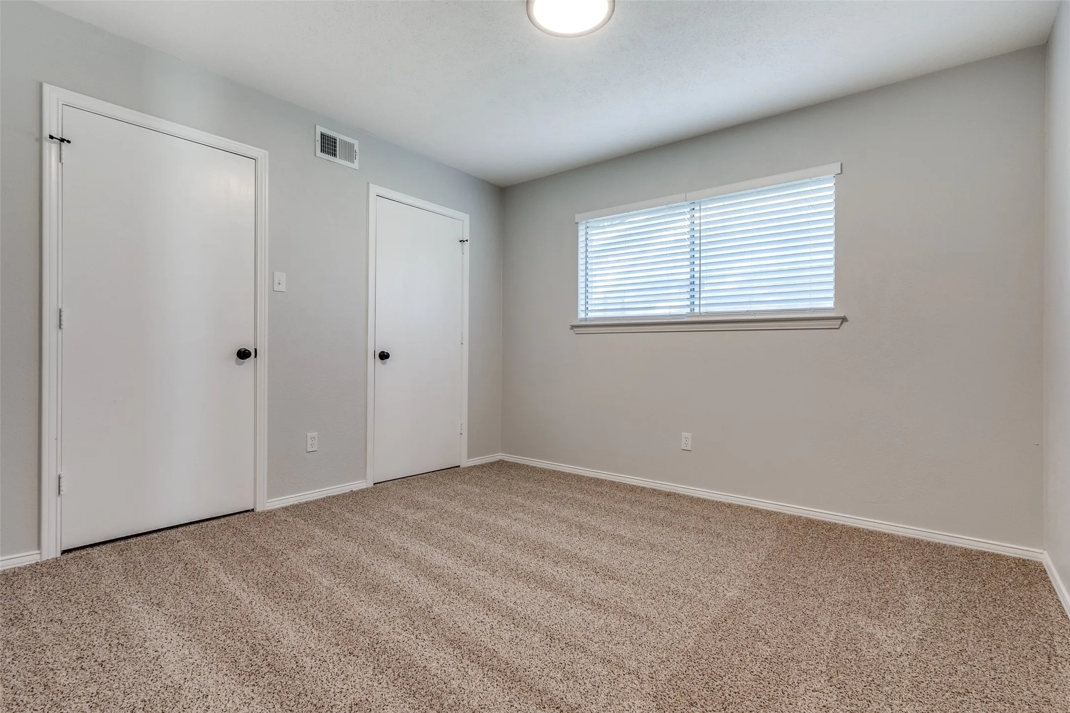 Spacious room featuring neutral carpeting, light gray wall paint, and white trim