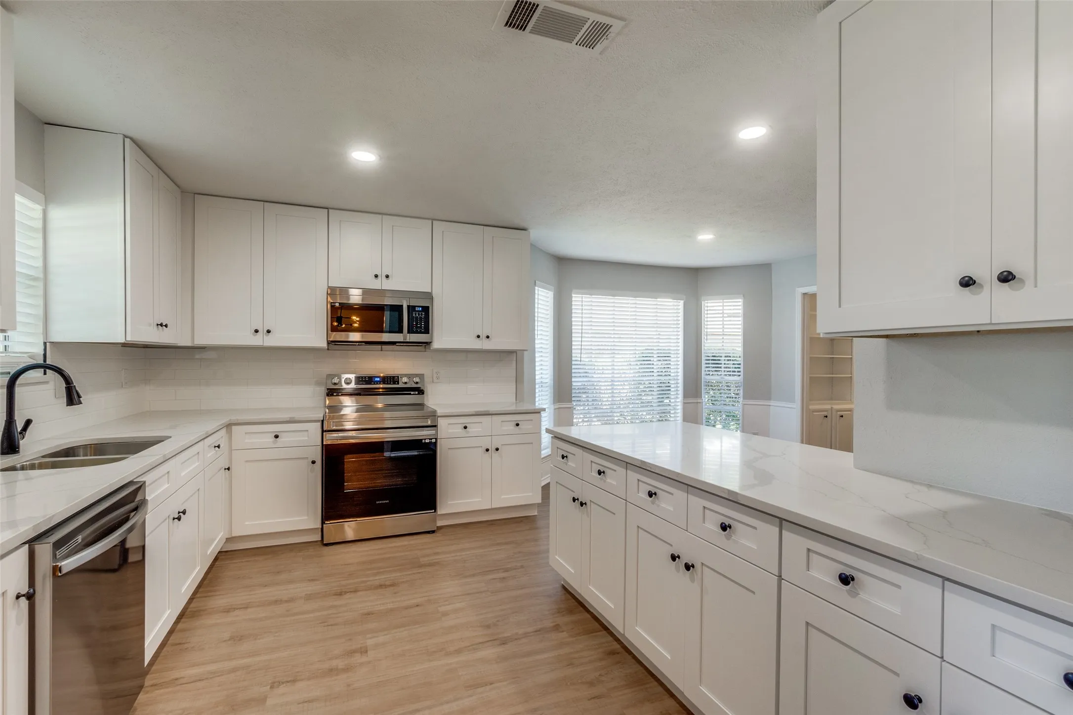 Modern kitchen featuring white shaker cabinetry, stainless steel appliances, quartz countertops, wood-finish flooring, and recessed lighting