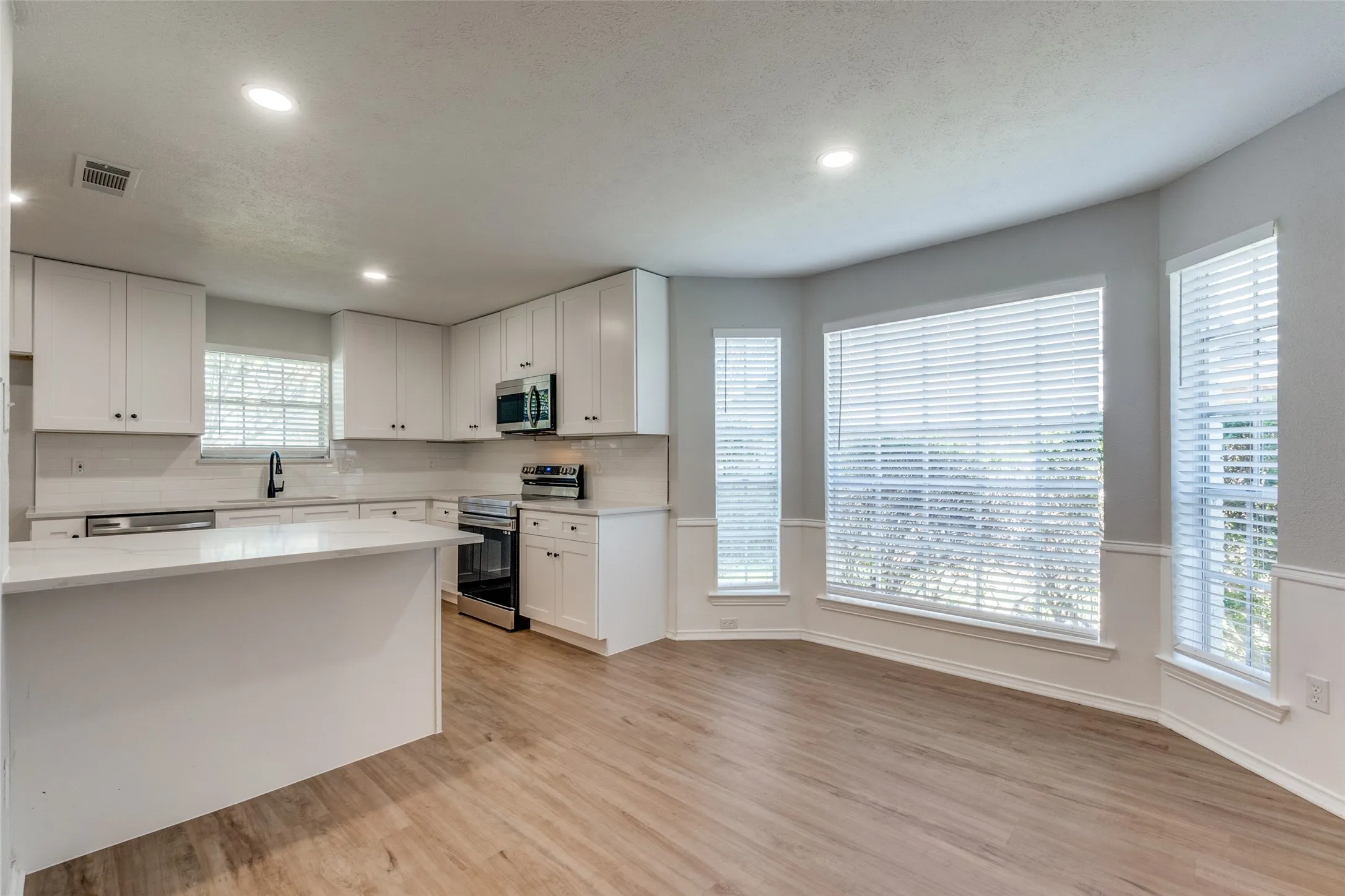 Modern kitchen featuring white cabinetry, stainless steel appliances, a large island, wood-finish flooring, and ample natural light from multiple windows