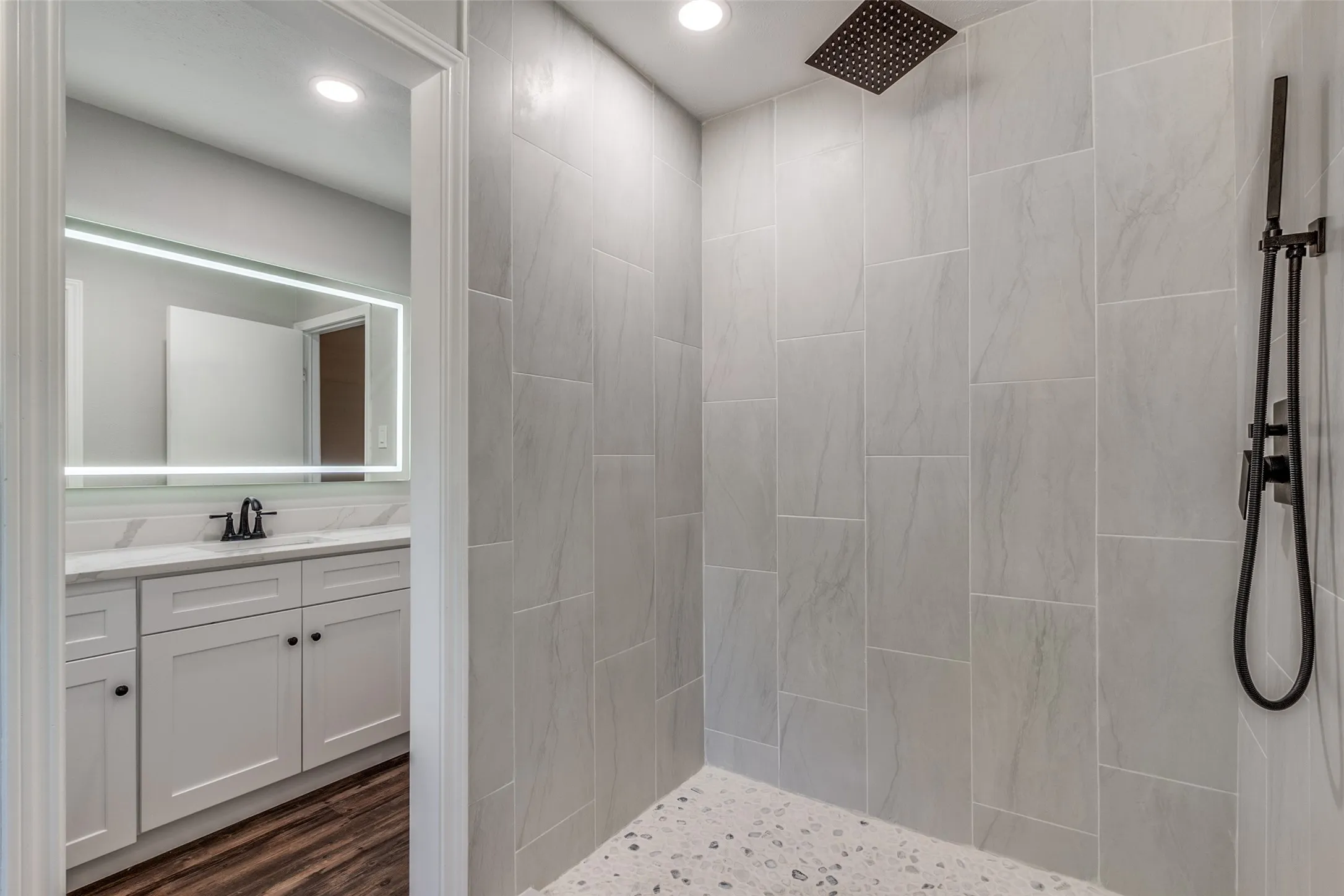 Walk-in shower featuring light-toned large format tile, a rain showerhead, and a handheld shower unit with matte black fixtures