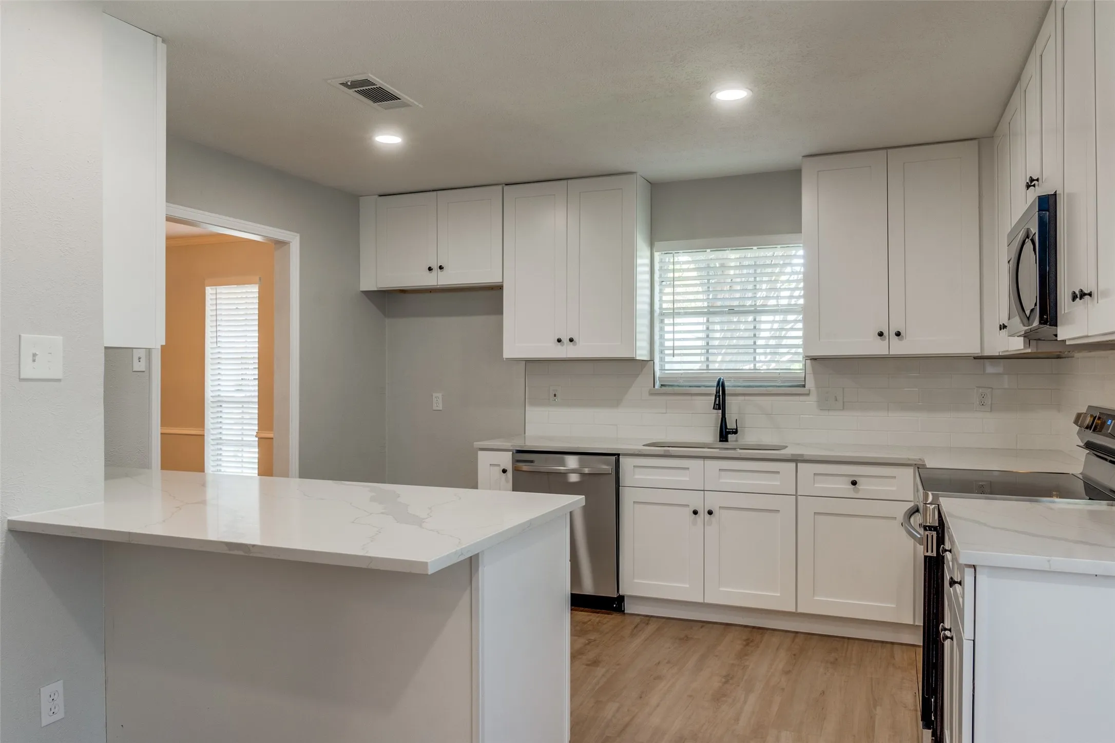 Modern kitchen featuring white shaker cabinetry, stainless steel appliances, a white subway tile backsplash, and light wood-finish flooring