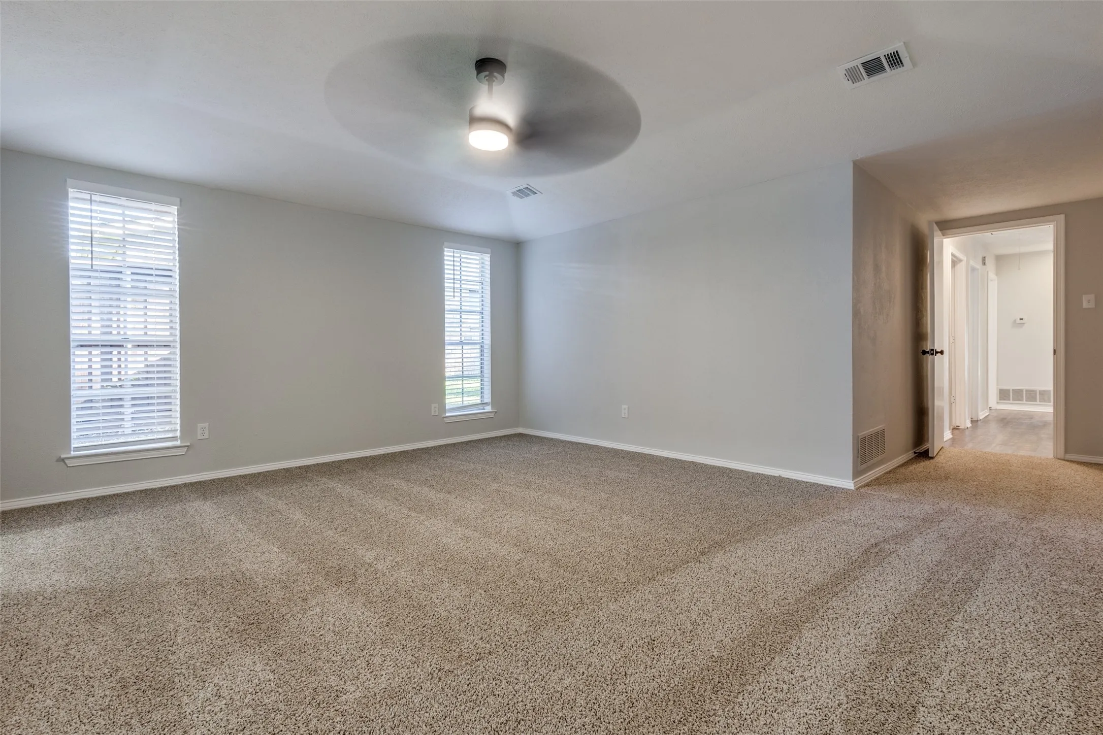 Spacious room featuring neutral carpeting, light-toned walls, and a modern ceiling fan with integrated lighting