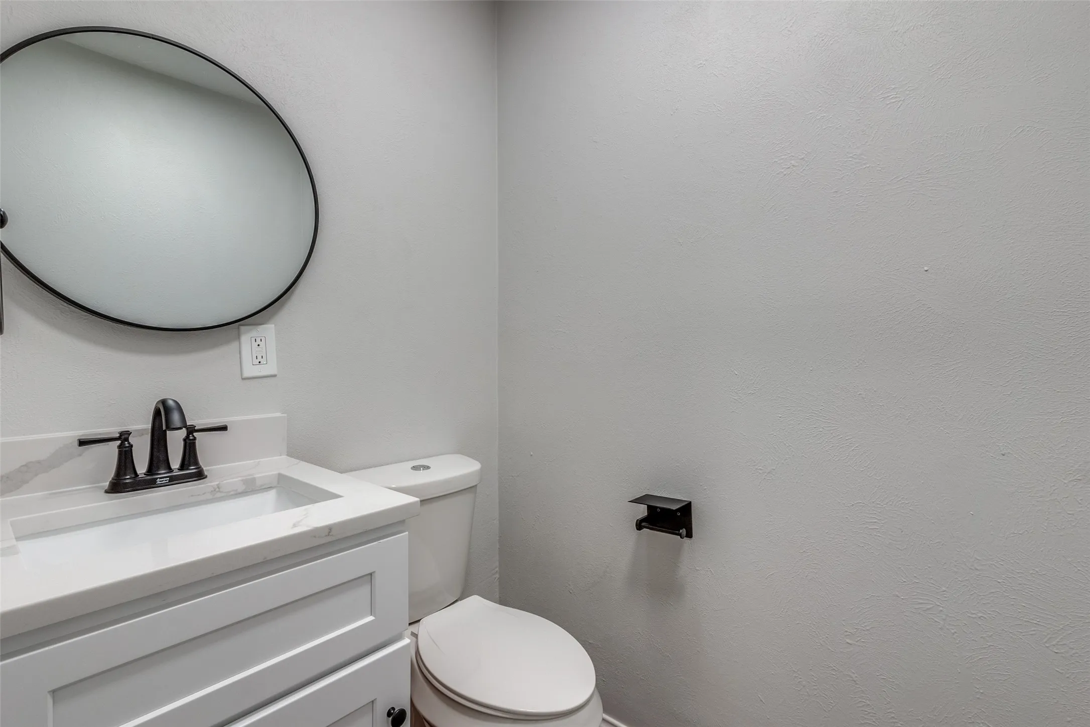 Bathroom featuring a white vanity with a rectangular basin, black faucet, and a round black-framed mirror