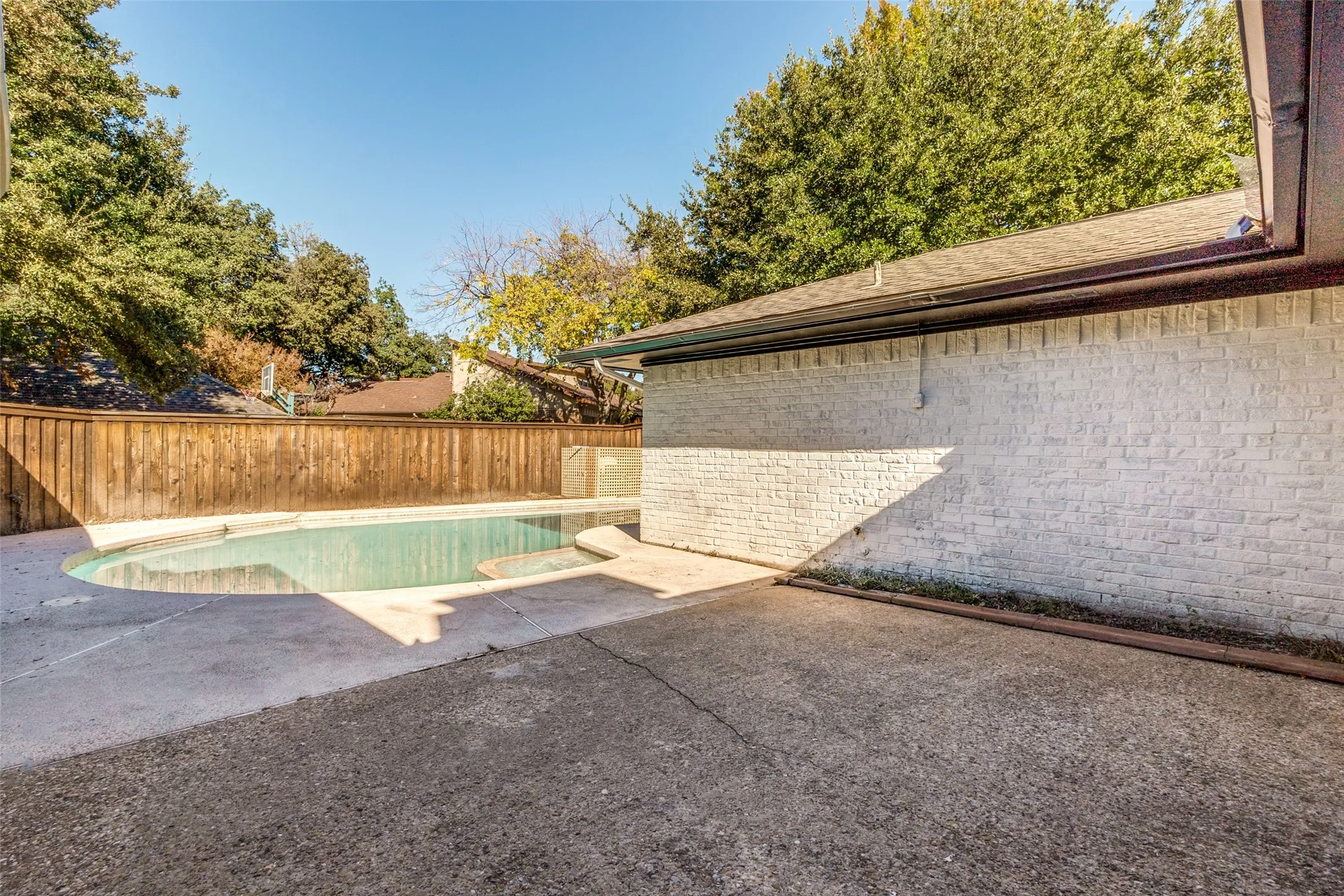 Backyard swimming pool with concrete decking, surrounded by a wood privacy fence and mature trees