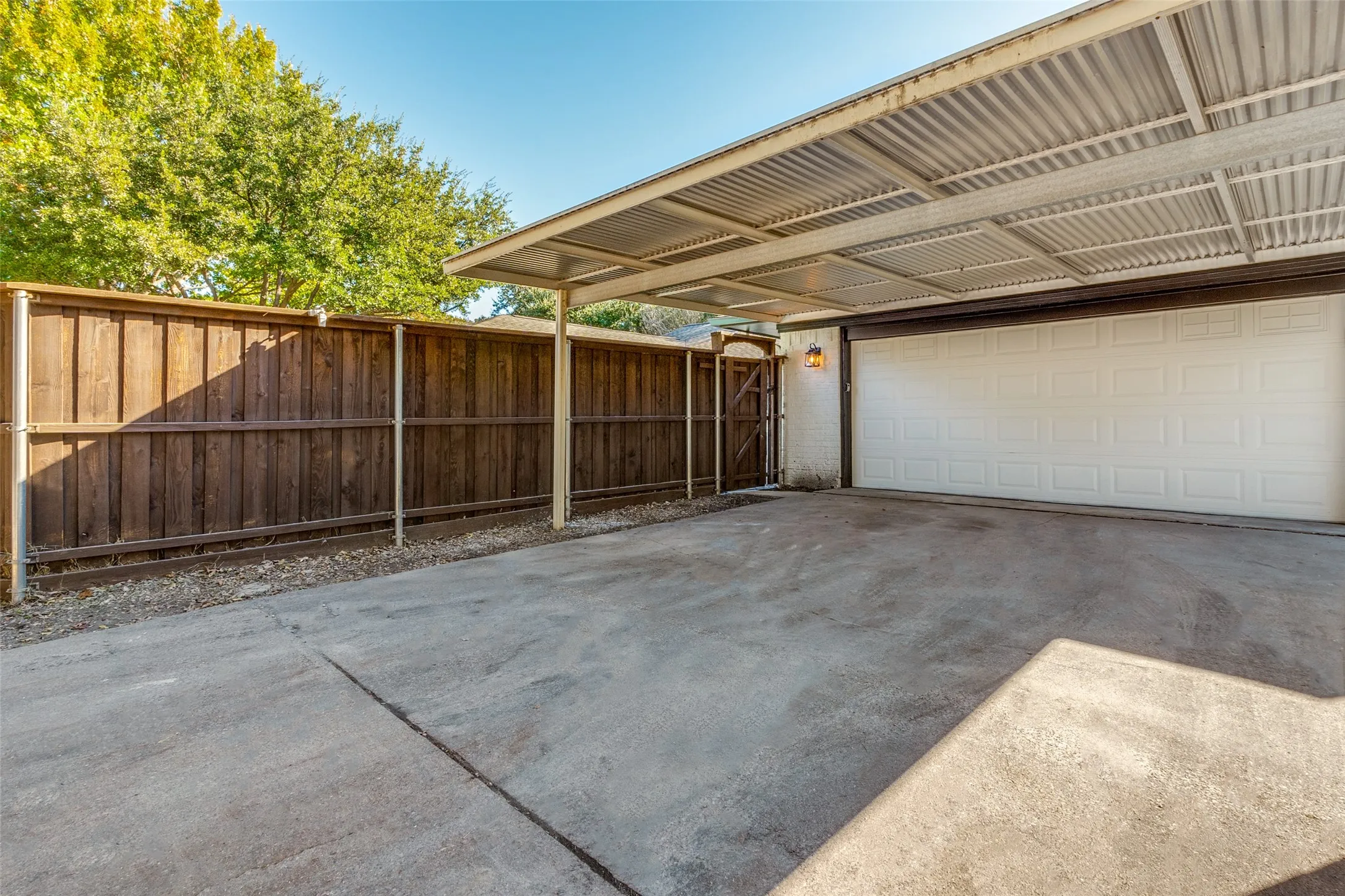 Covered carport with a corrugated metal roof, concrete driveway, and white panel garage door