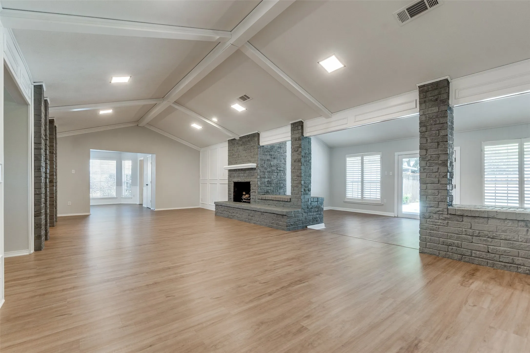 Spacious living area featuring wood-finish flooring, a vaulted ceiling with exposed beams, and recessed lighting