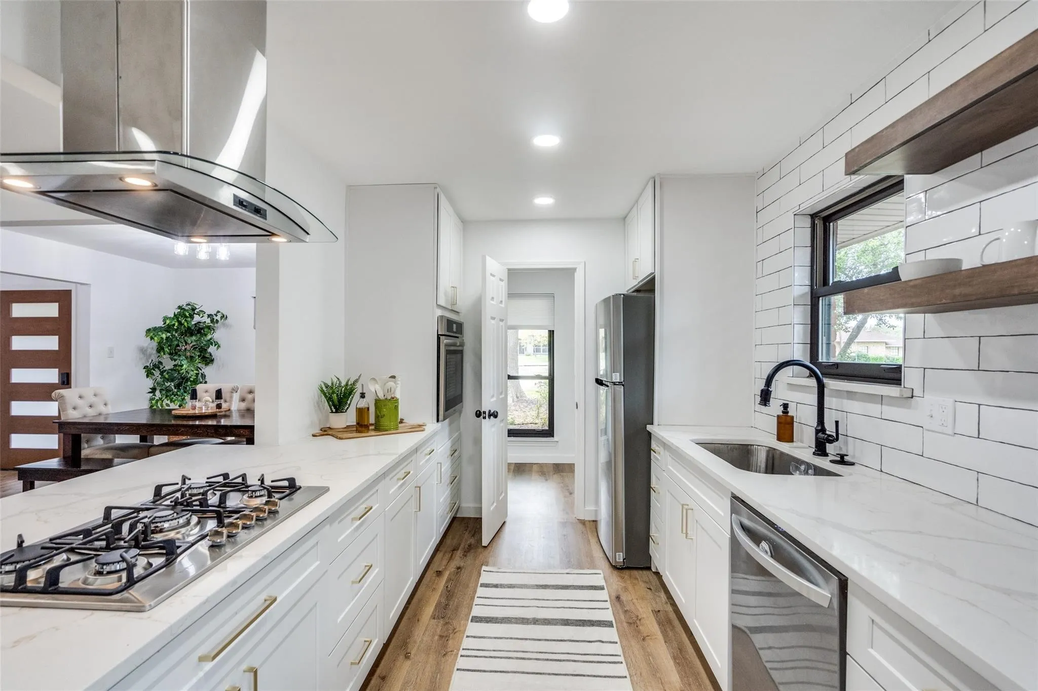 White kitchen featuring extensive counter space, a built-in gas cooktop with an overhead range hood, white subway tile backsplash, and wood-finish flooring