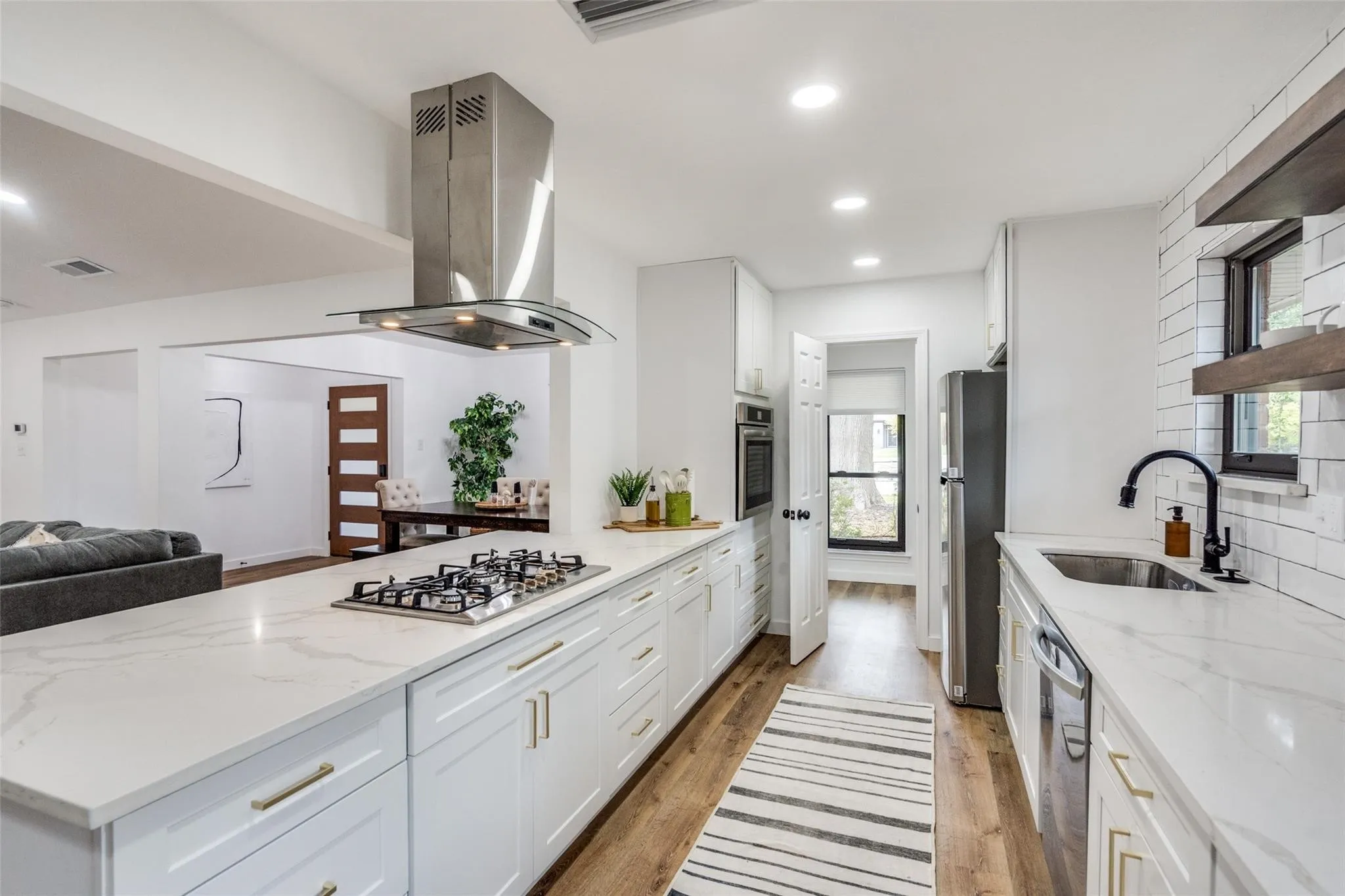 Modern kitchen featuring white cabinetry, light countertops, wood-finish flooring, a stainless steel range hood, and a built-in cooktop