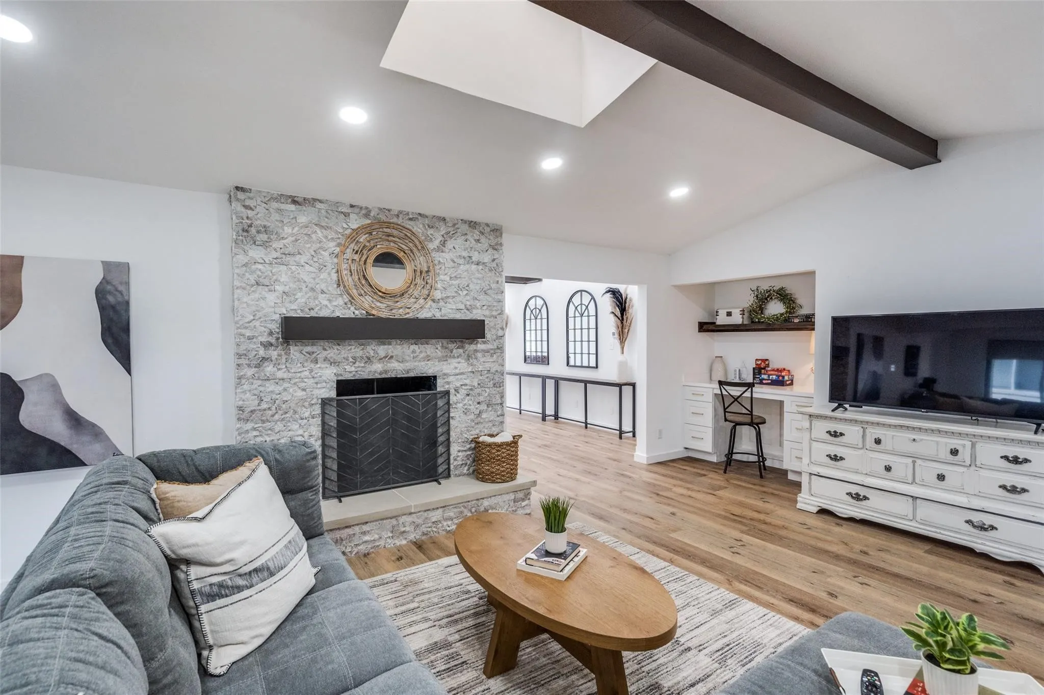 Living area featuring a stone-clad fireplace with a hearth, wood-finish flooring, a vaulted ceiling with exposed beam, recessed lighting, and a built-in desk area