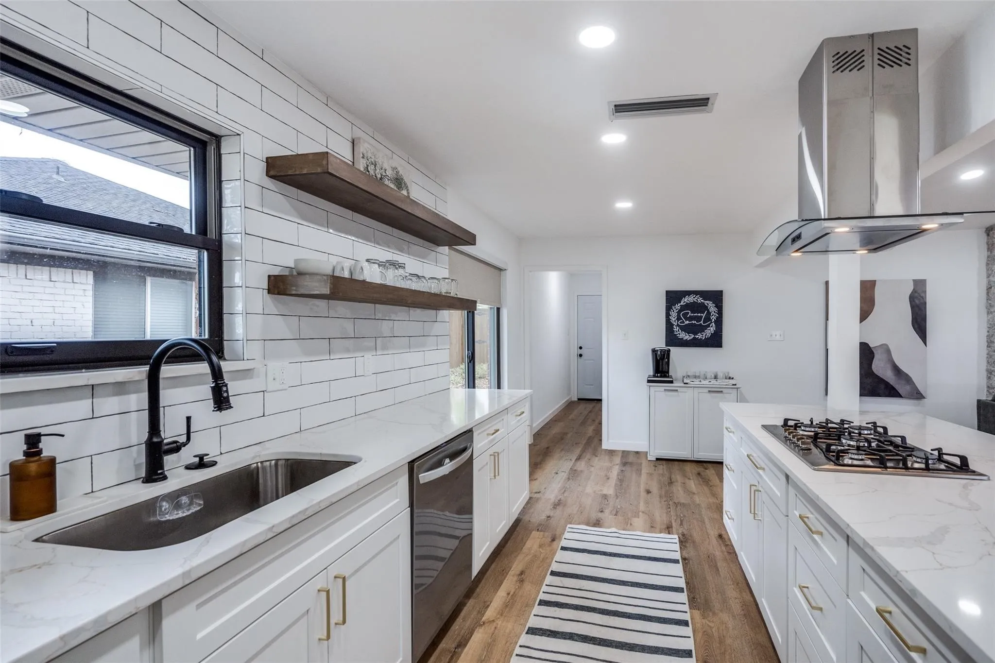 Modern kitchen featuring white shaker cabinetry, light wood-finish flooring, white subway tile backsplash, and a stainless steel gas range with a matching range hood