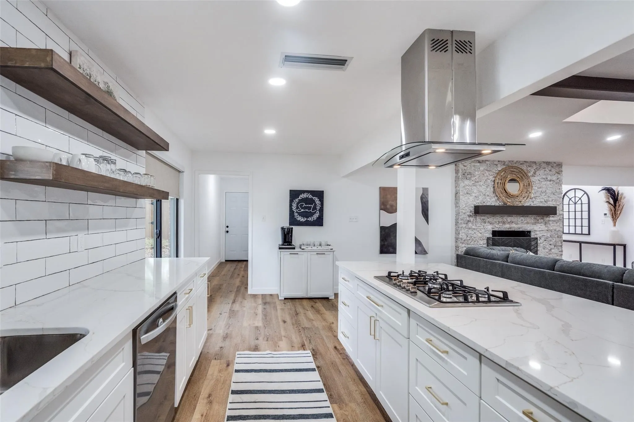 Modern kitchen featuring white shaker cabinetry, wood-finish flooring, white subway tile backsplash, and a large central island with an integrated cooktop