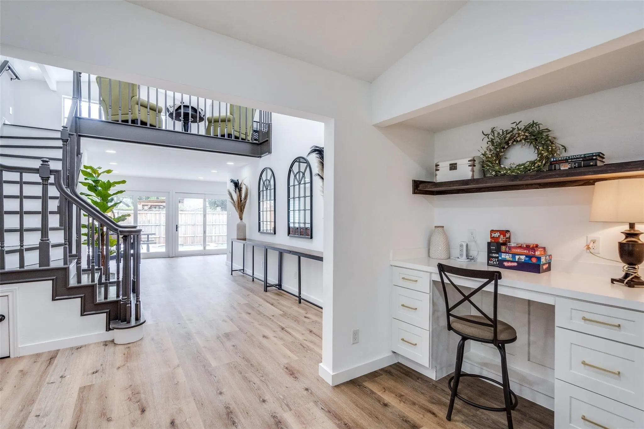 Open-concept interior featuring wood-finish flooring, a grand staircase with dark railings, a built-in desk with white cabinetry, and multiple sliding glass doors at the rear