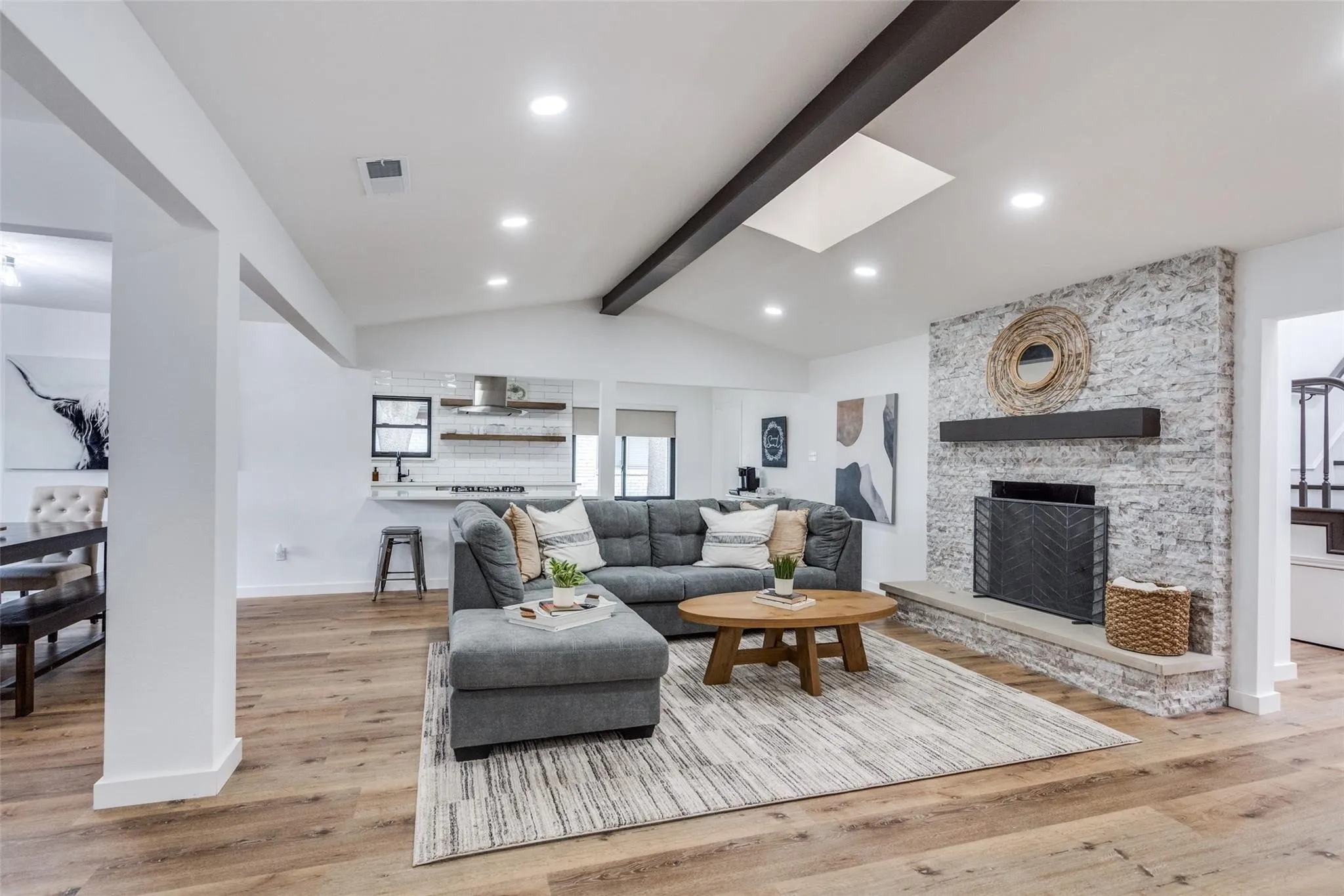 Spacious living area featuring wood-finish flooring, a vaulted ceiling with exposed beam, and a skylight
