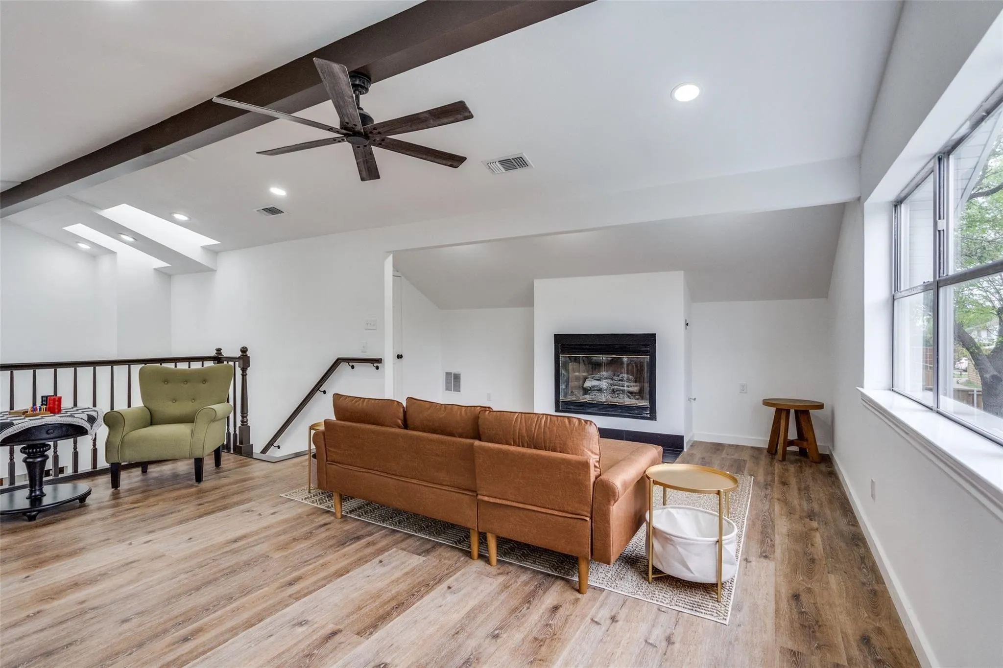 Spacious living area featuring wood-finish flooring, exposed ceiling beams, a fireplace, and large windows