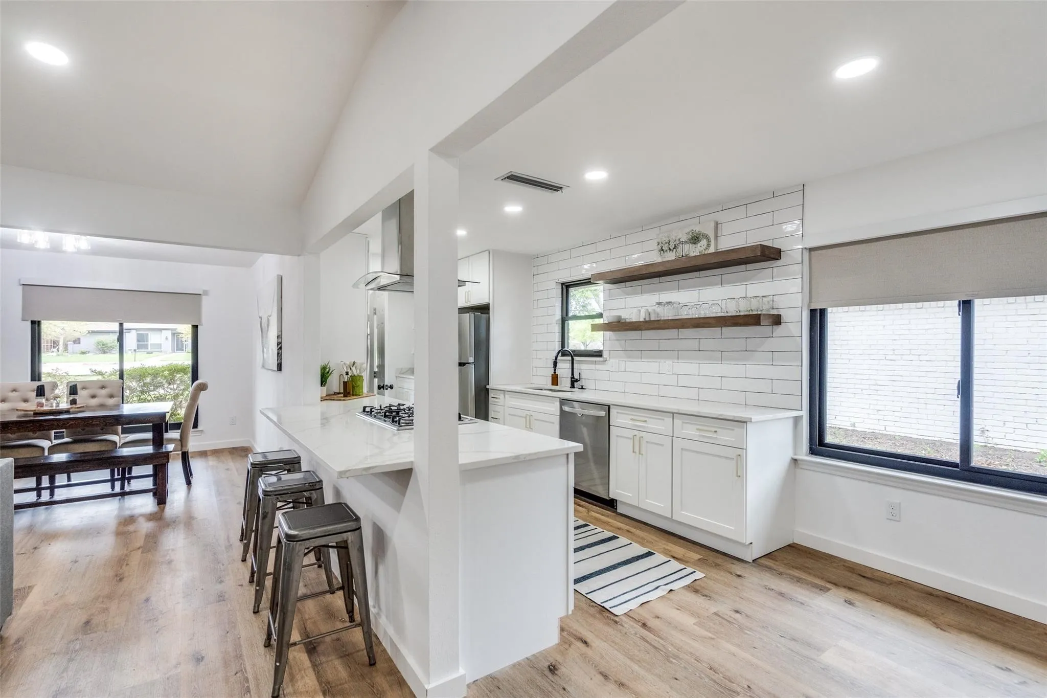 Modern kitchen featuring white shaker cabinetry, white subway tile backsplash, stainless steel appliances, a kitchen island with seating, and wood-finish flooring