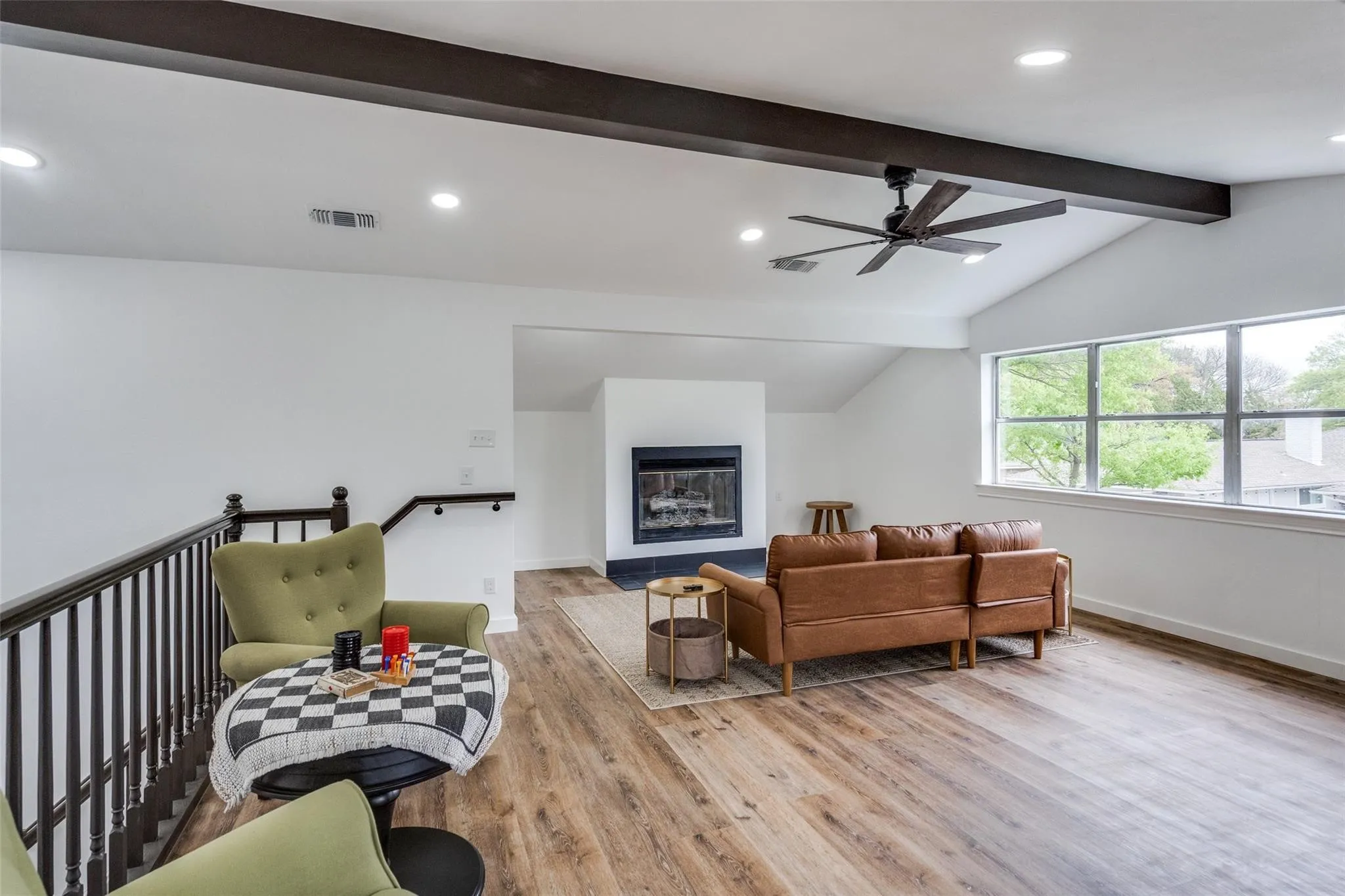Spacious loft featuring wood-finish flooring, a contemporary fireplace with a black surround, and a vaulted ceiling with exposed beams