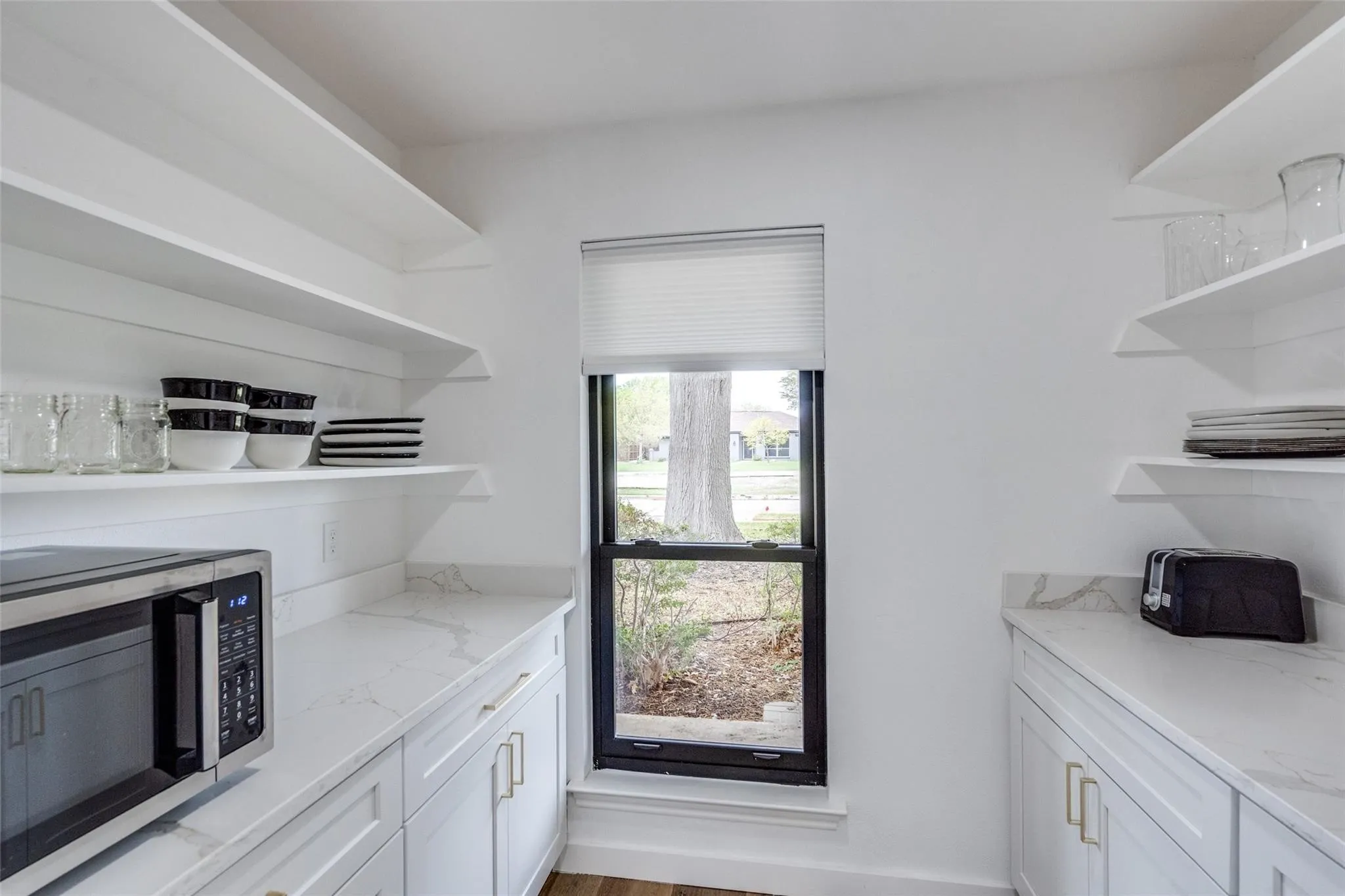 Spacious pantry featuring white cabinetry, light countertops, open shelving, and a black-framed window