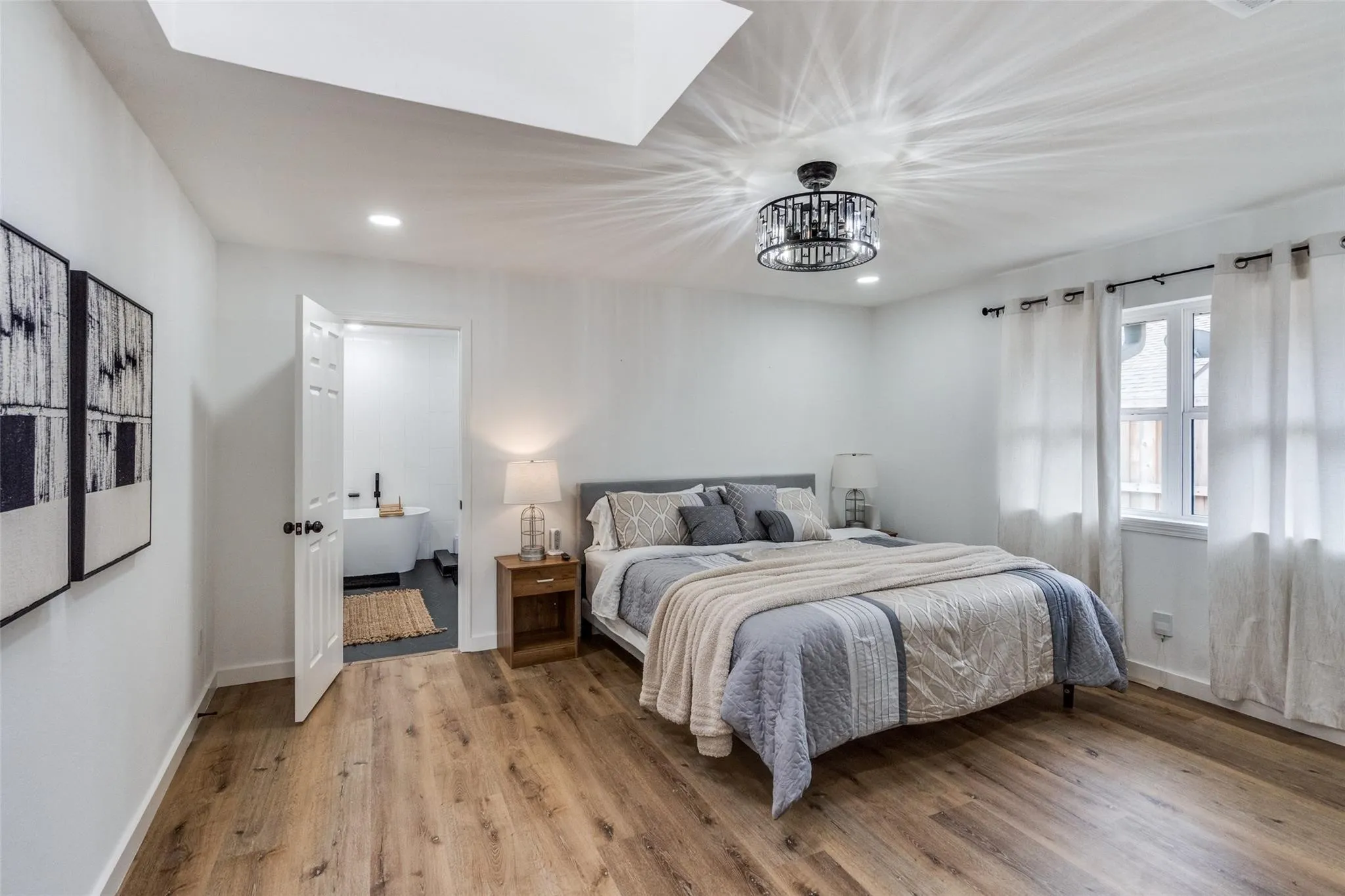 Bedroom featuring wood-finish flooring, a contemporary ceiling light fixture, and an open doorway leading to a bathroom with a freestanding tub