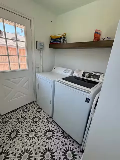 downstairs Dedicated laundry area featuring patterned tile flooring, a white paneled exterior door with window panes, and a wood-finish floating shelf