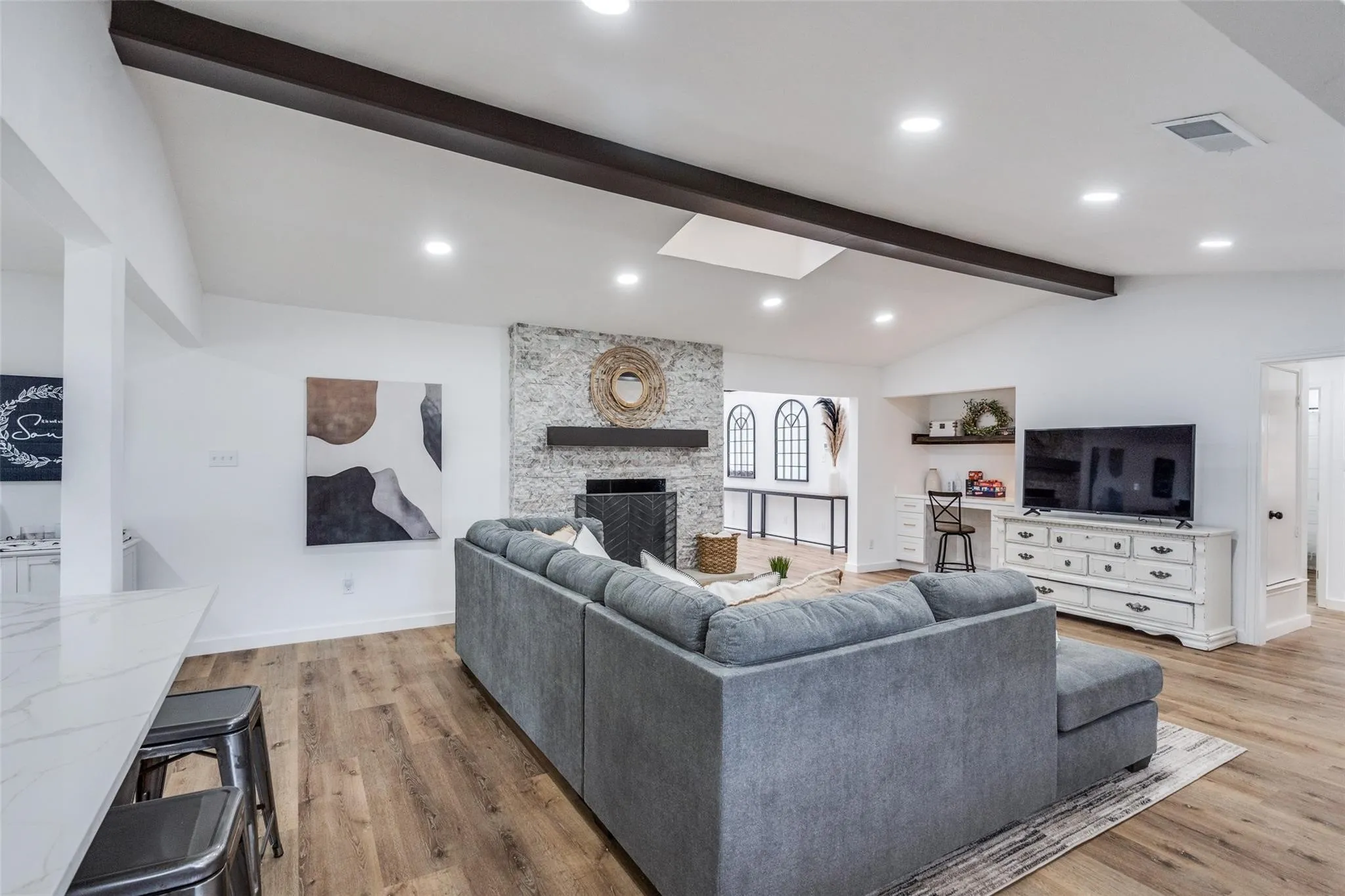 Vaulted ceiling with dark wood beams, skylight, recessed lighting, stone fireplace, and wood-finish flooring