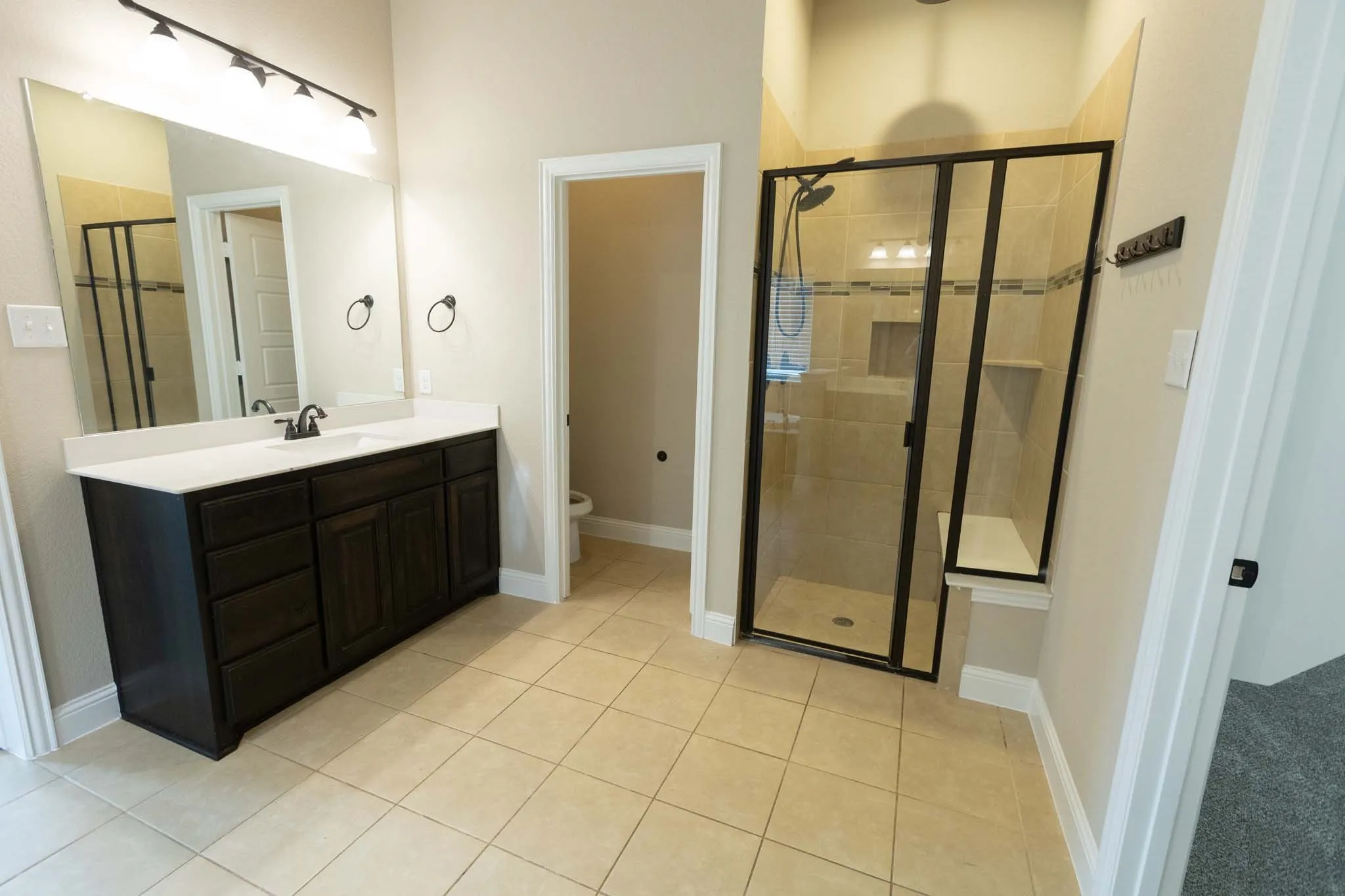 Expansive bathroom featuring a dark wood finish double vanity with a white countertop, large wall-mounted mirror, and a glass-enclosed shower with a built-in bench