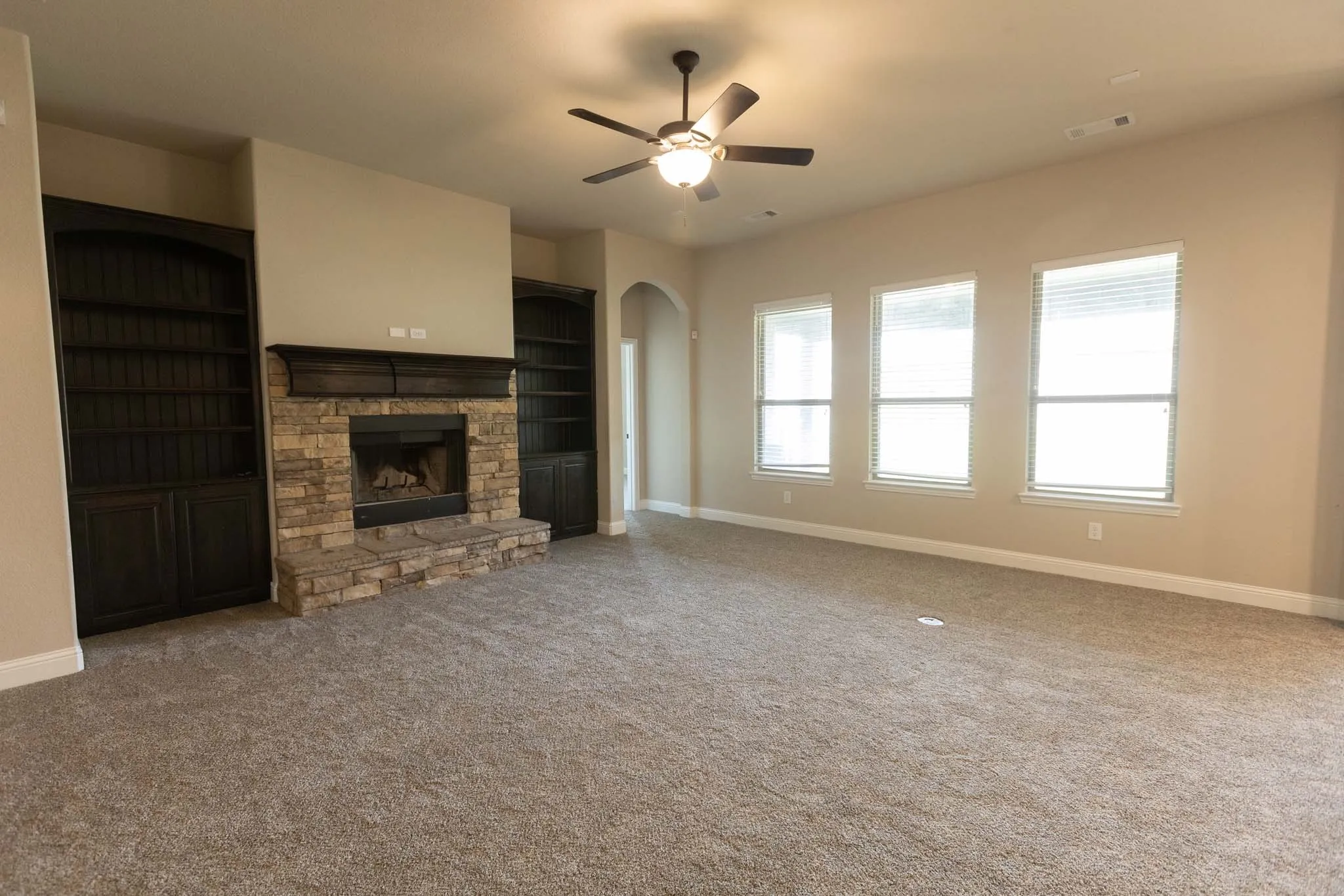 Spacious living area featuring a stone-clad fireplace with a dark wood mantel, flanked by built-in dark wood bookshelves with lower cabinetry