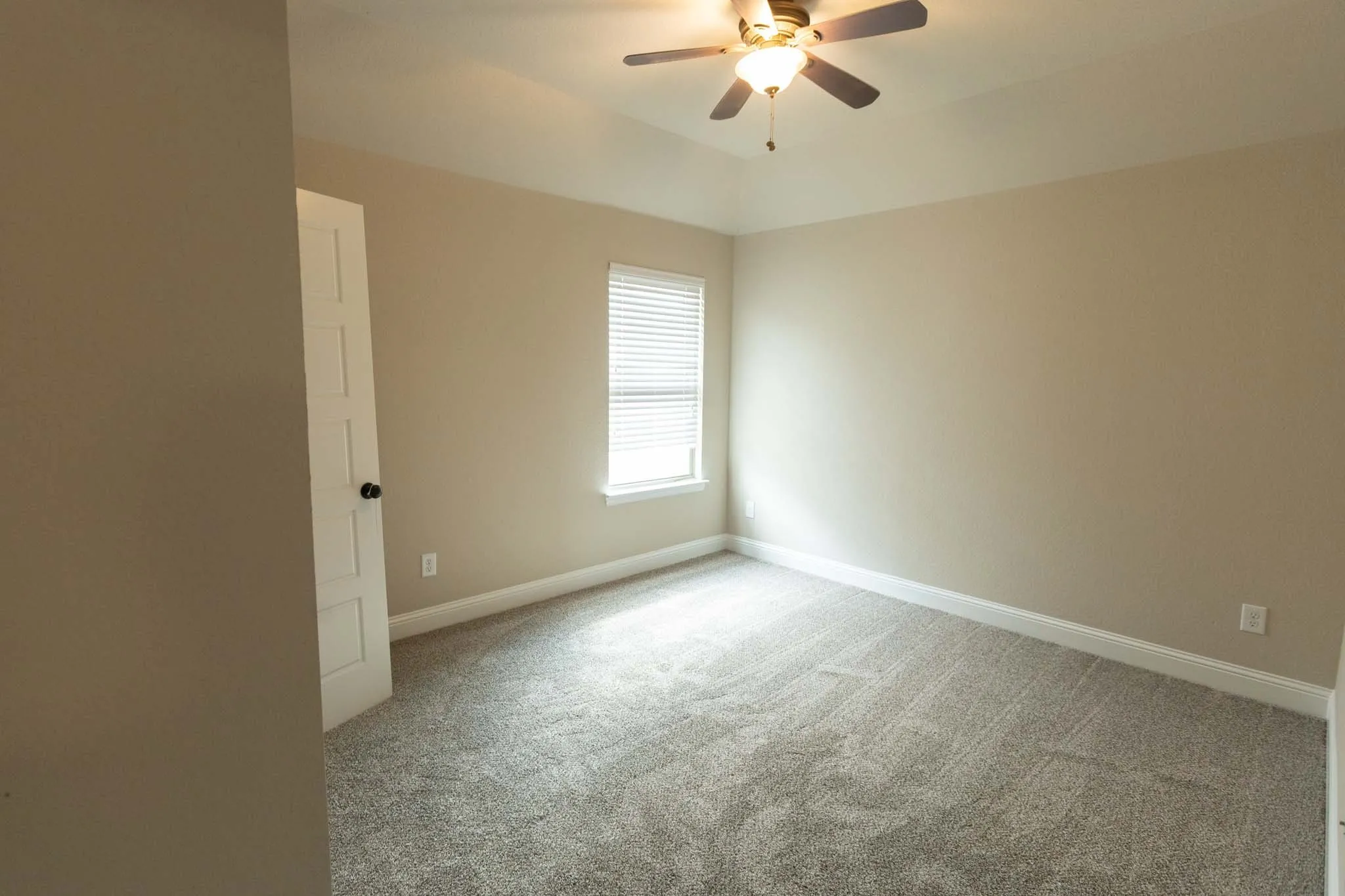 Upstairs Carpeted interior room featuring a tray ceiling with a ceiling fan, a window with horizontal blinds, and a white paneled door with a black knob
