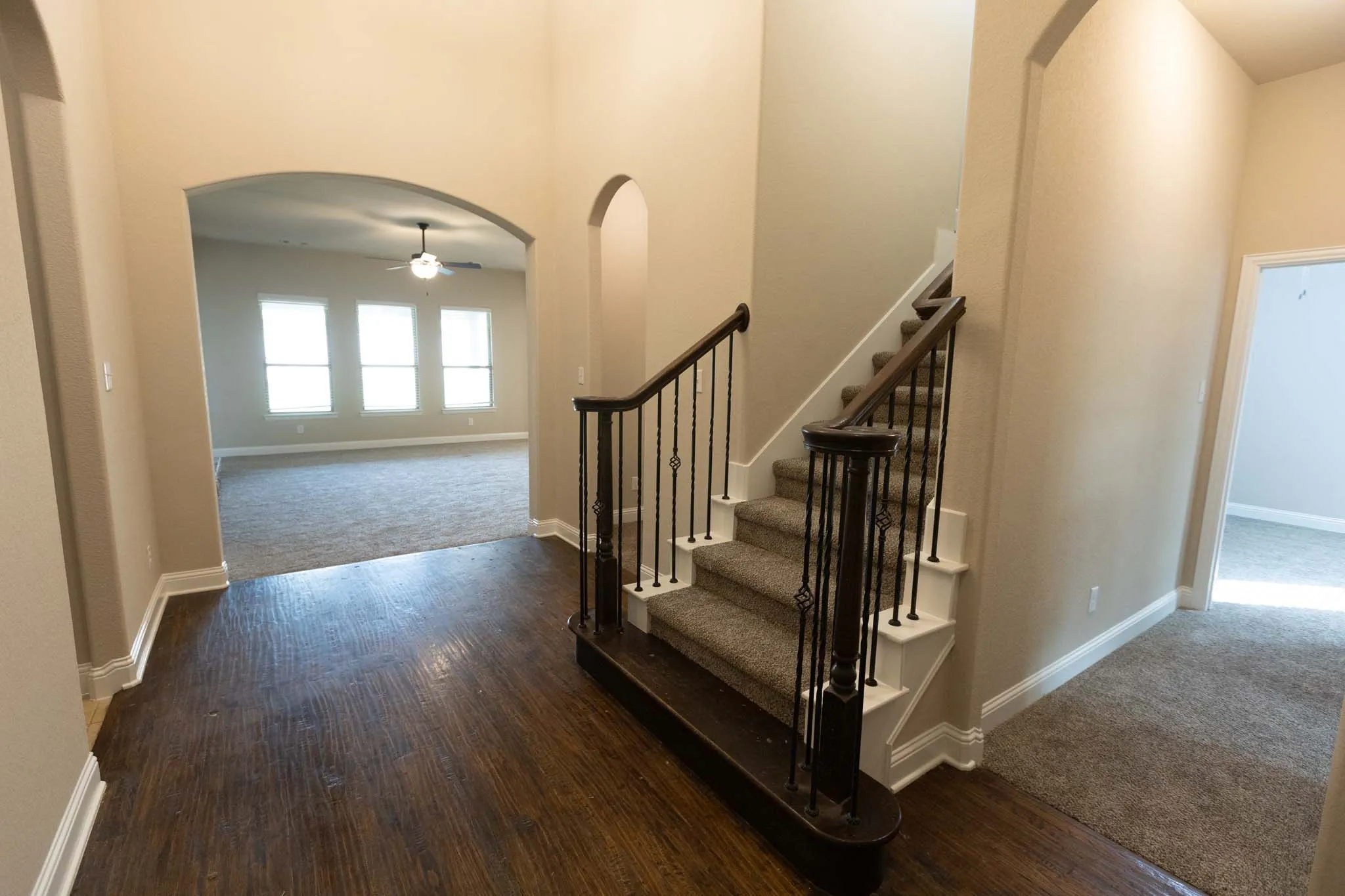 Expansive entryway featuring wood-finish flooring, a carpeted staircase with wrought iron balusters, and arched doorways