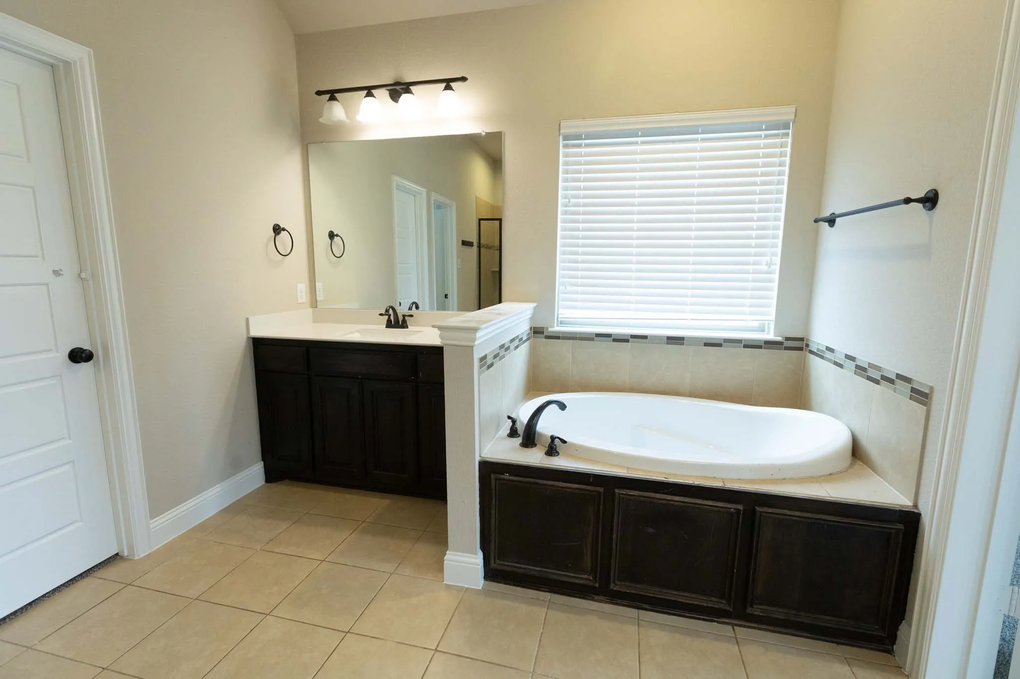 Primary Bathroom featuring a built-in soaking tub, a single vanity with dark wood cabinetry, a large mirror, and tiled flooring