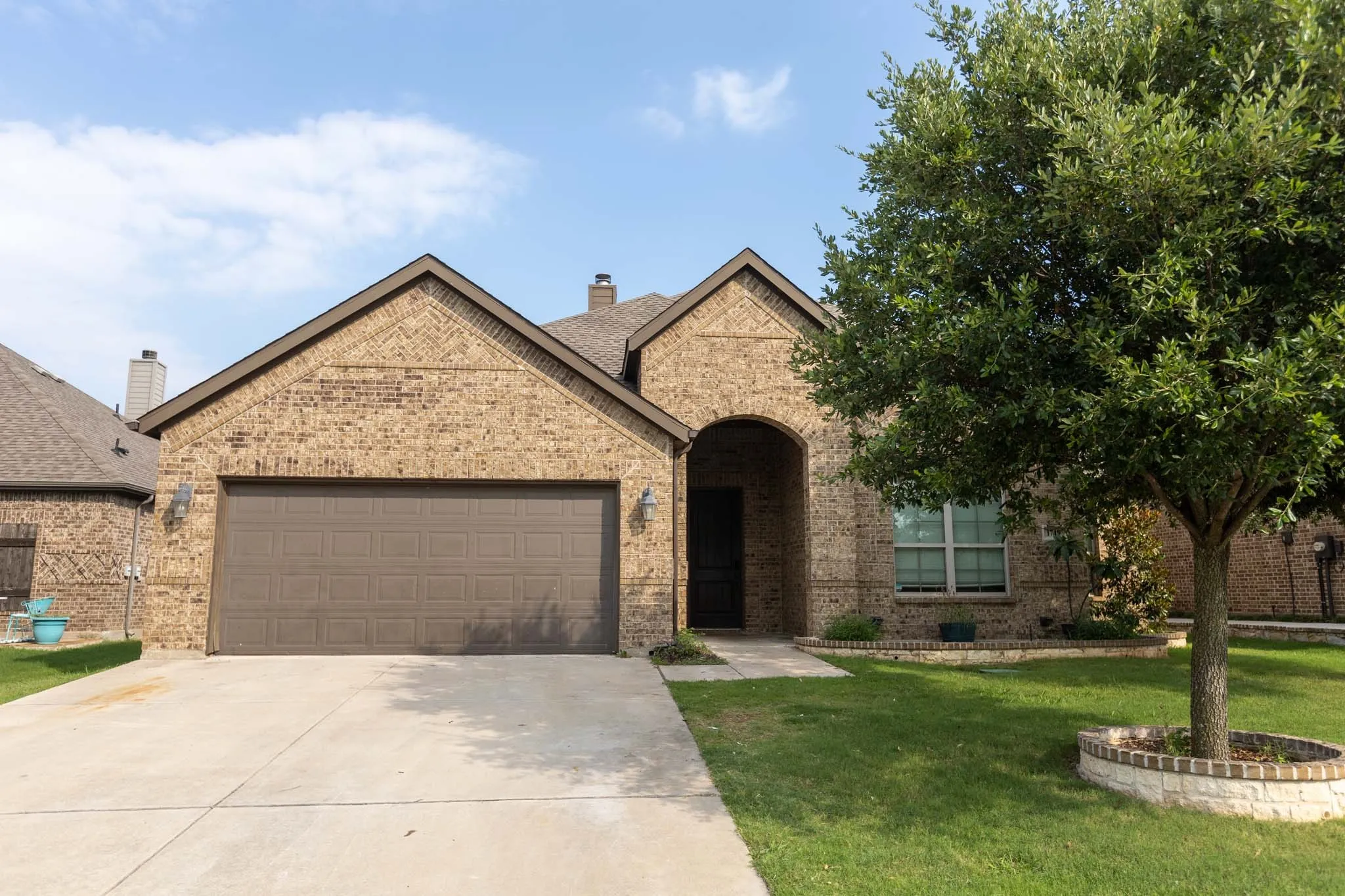 Brick exterior with a prominent two-car garage, an arched entryway, and a mature tree