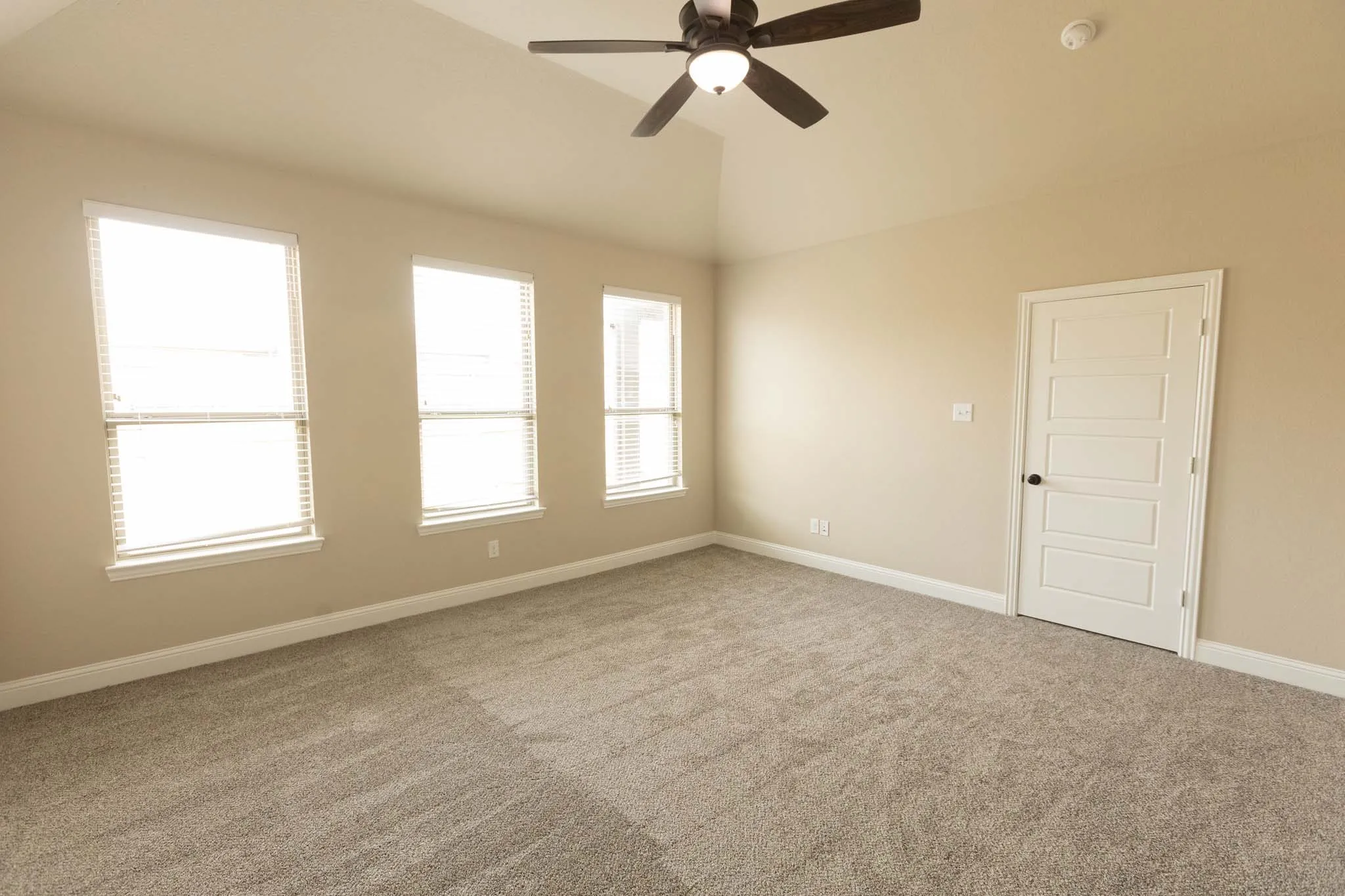 Spacious room featuring vaulted ceilings, a ceiling fan with integrated lighting, and three large windows with blinds