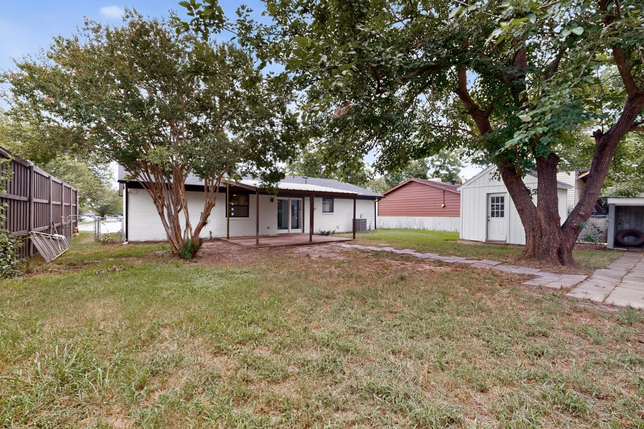 Backyard featuring a white exterior home with a covered patio, double glass doors, and mature trees