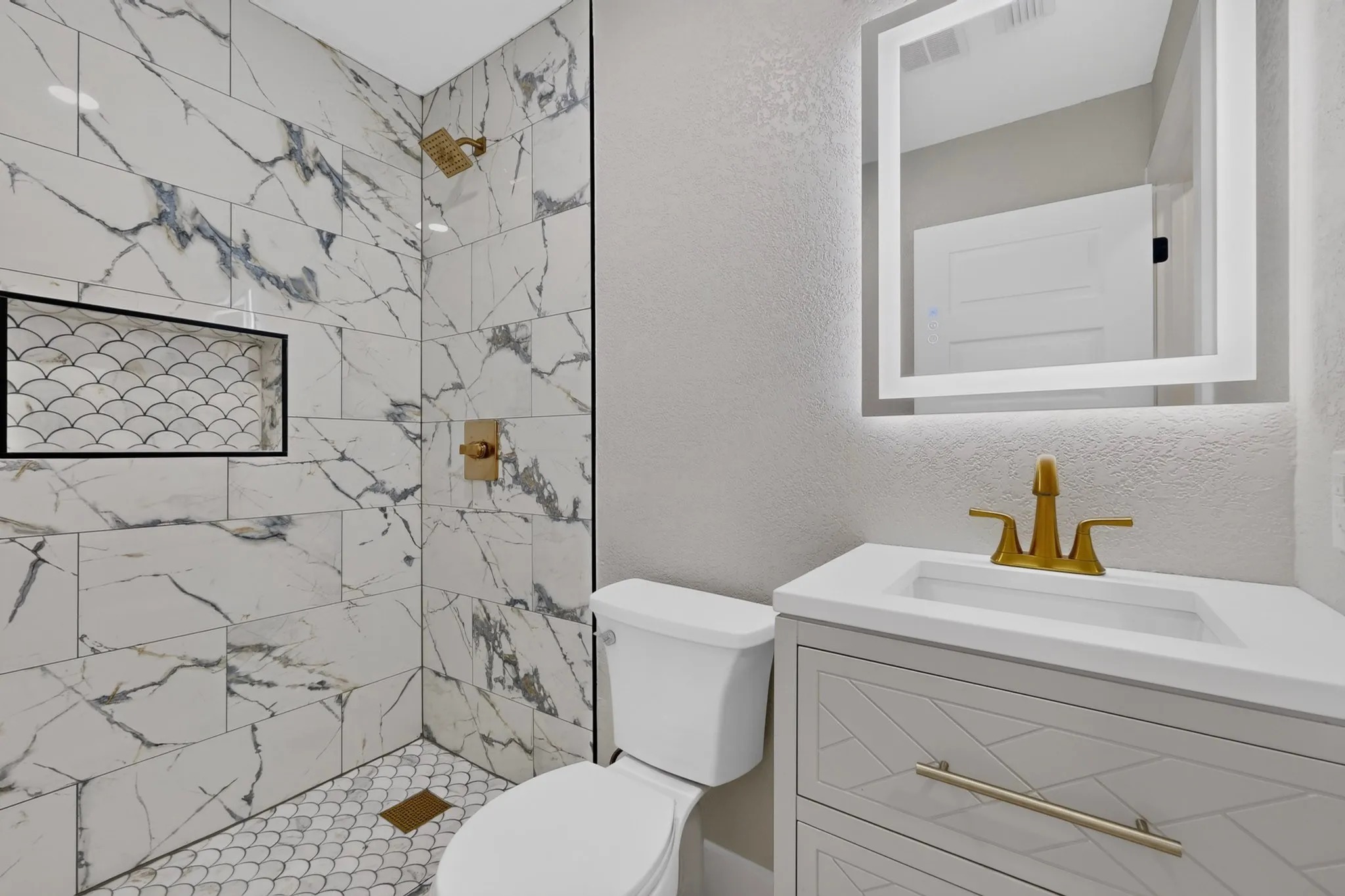 Bathroom featuring a shower with large format marble-look tile, a mosaic tile floor, and a recessed niche with black trim