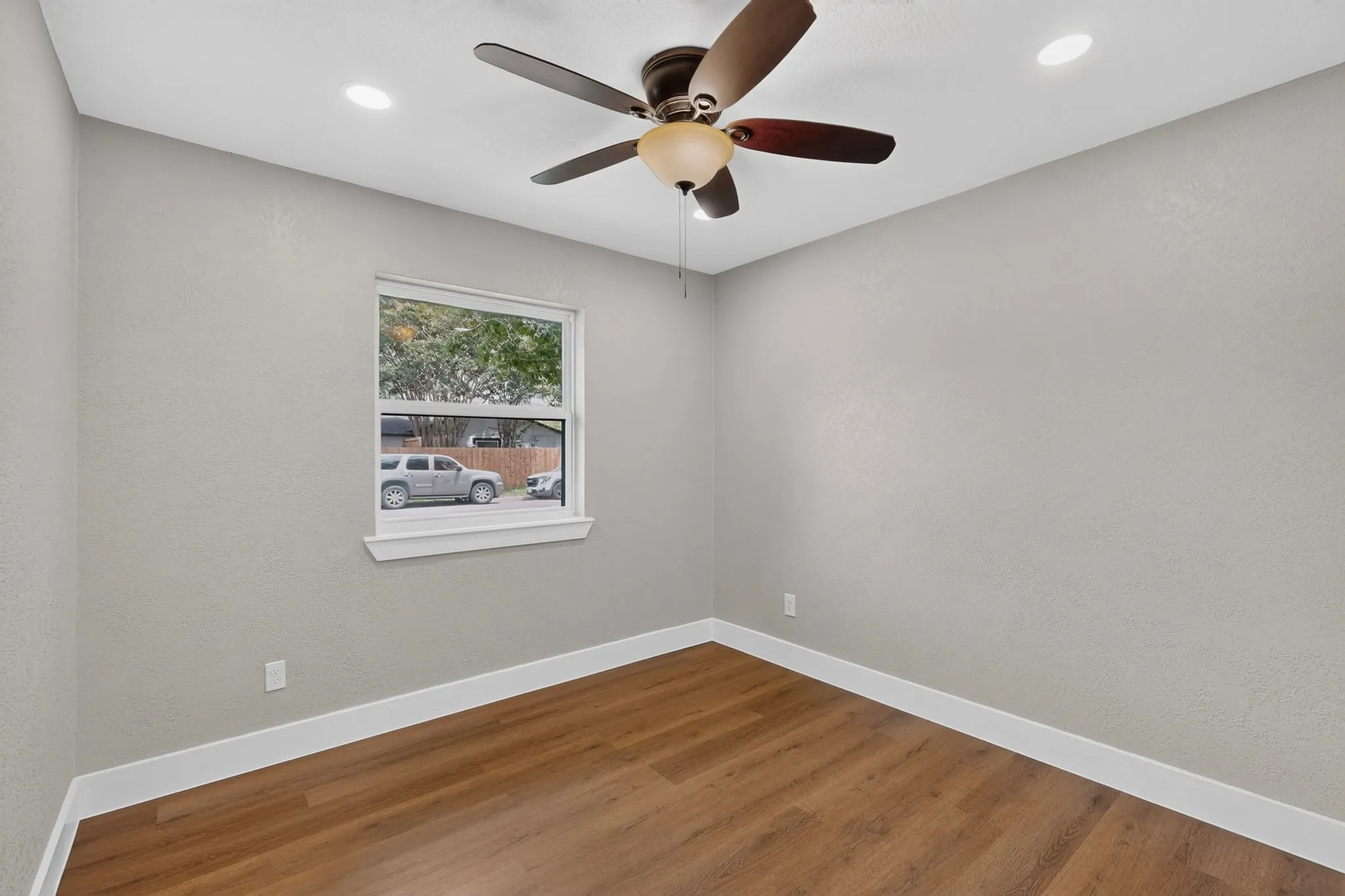 Bright room featuring wood-finish flooring, a ceiling fan with integrated lighting, recessed lighting, and a window with a white frame