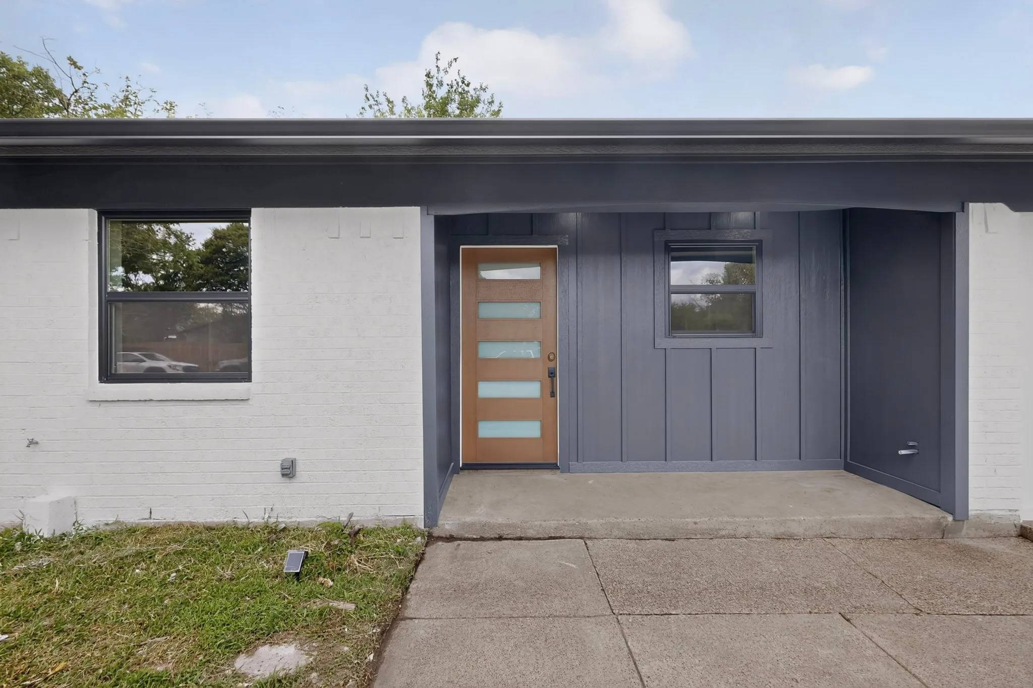 Modern entryway featuring a wood-panel door with frosted glass inserts, board and batten siding, and a concrete patio