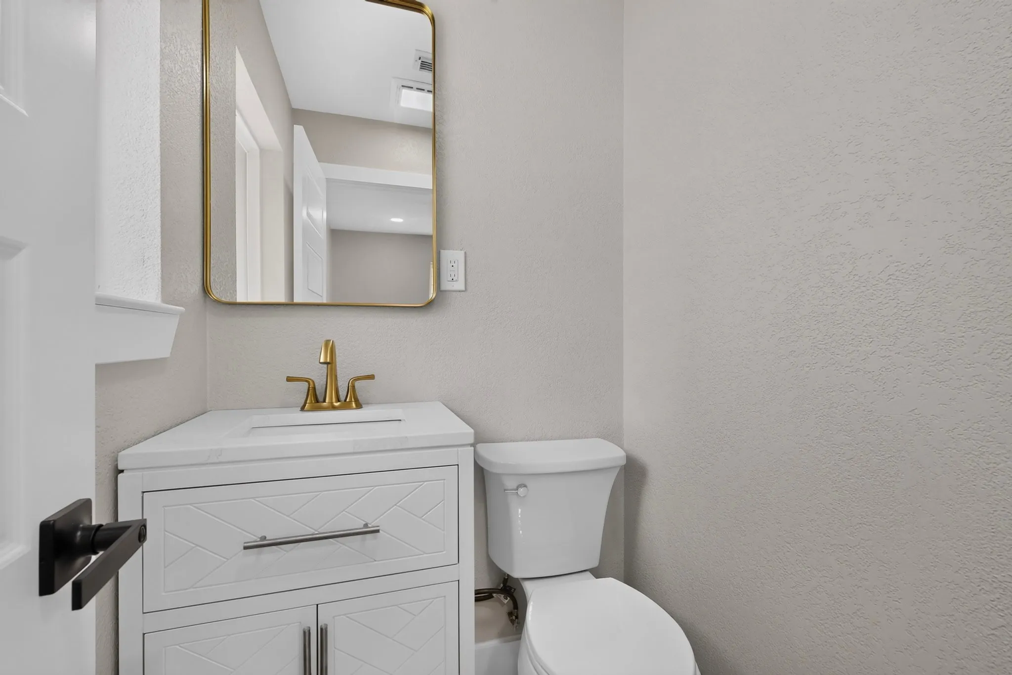 Bathroom featuring a white vanity with integrated sink, gold-finish faucet, and a rectangular mirror with a gold-tone frame
