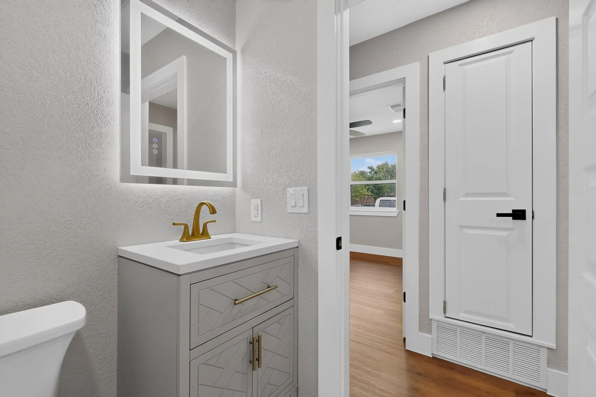 Bathroom vanity featuring a quartz countertop, gold-finish faucet, and a backlit mirror